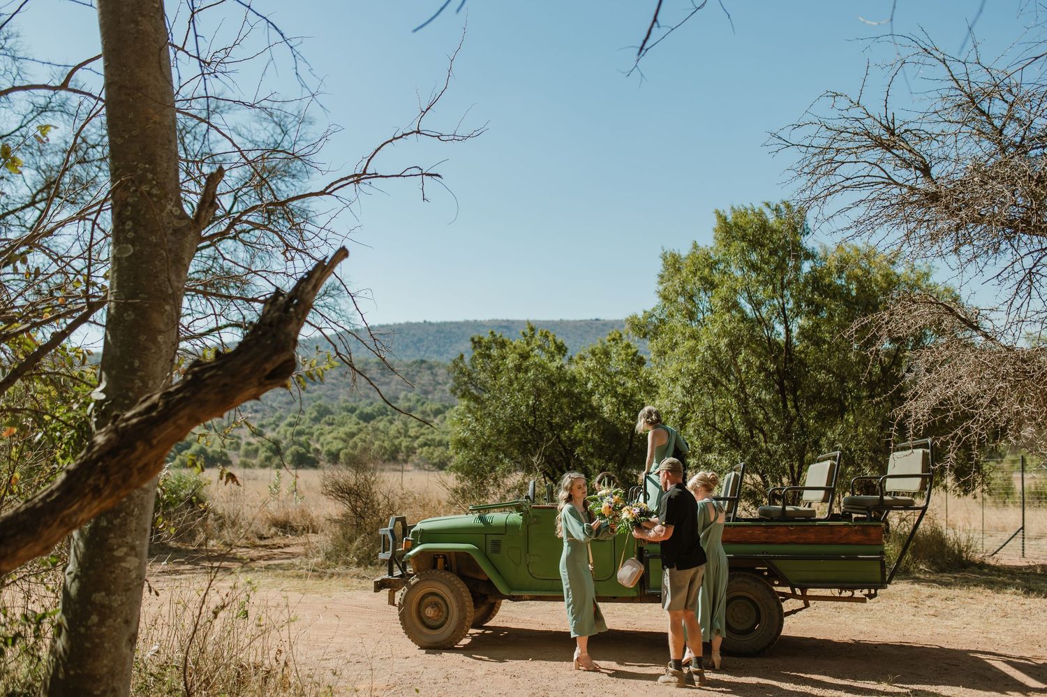 A vintage green off-road vehicle parked under trees in a rugged outdoor setting.