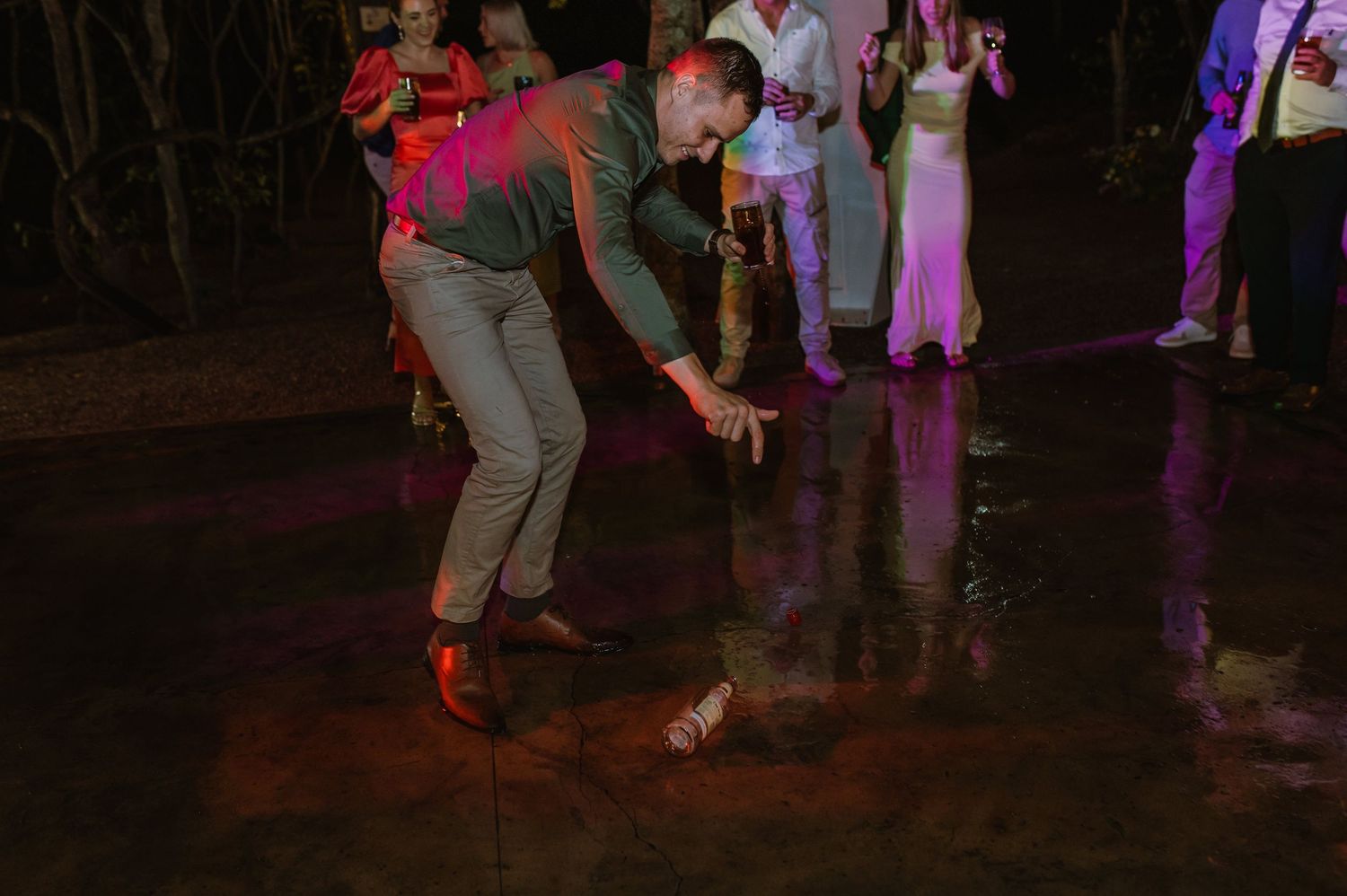 Wedding guest dancing energetically on reflective floor under colorful lights at reception.