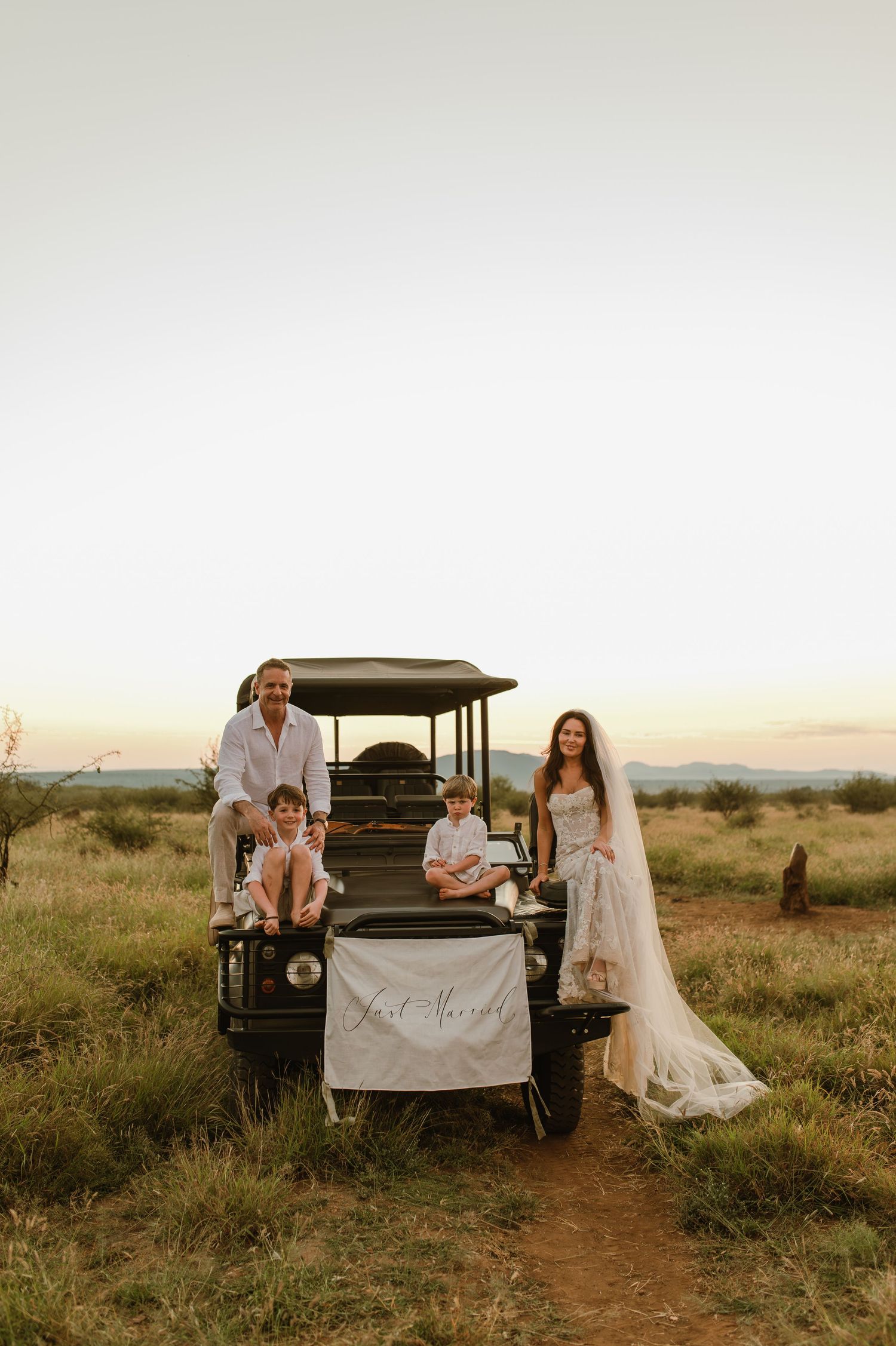 Just married couple with two children posing by safari vehicle at dusk.