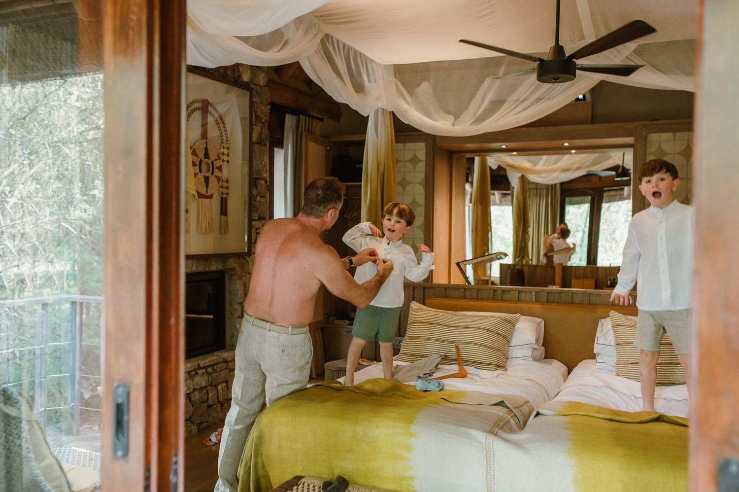 Father playing with two children on a bed in a luxury safari lodge bedroom.