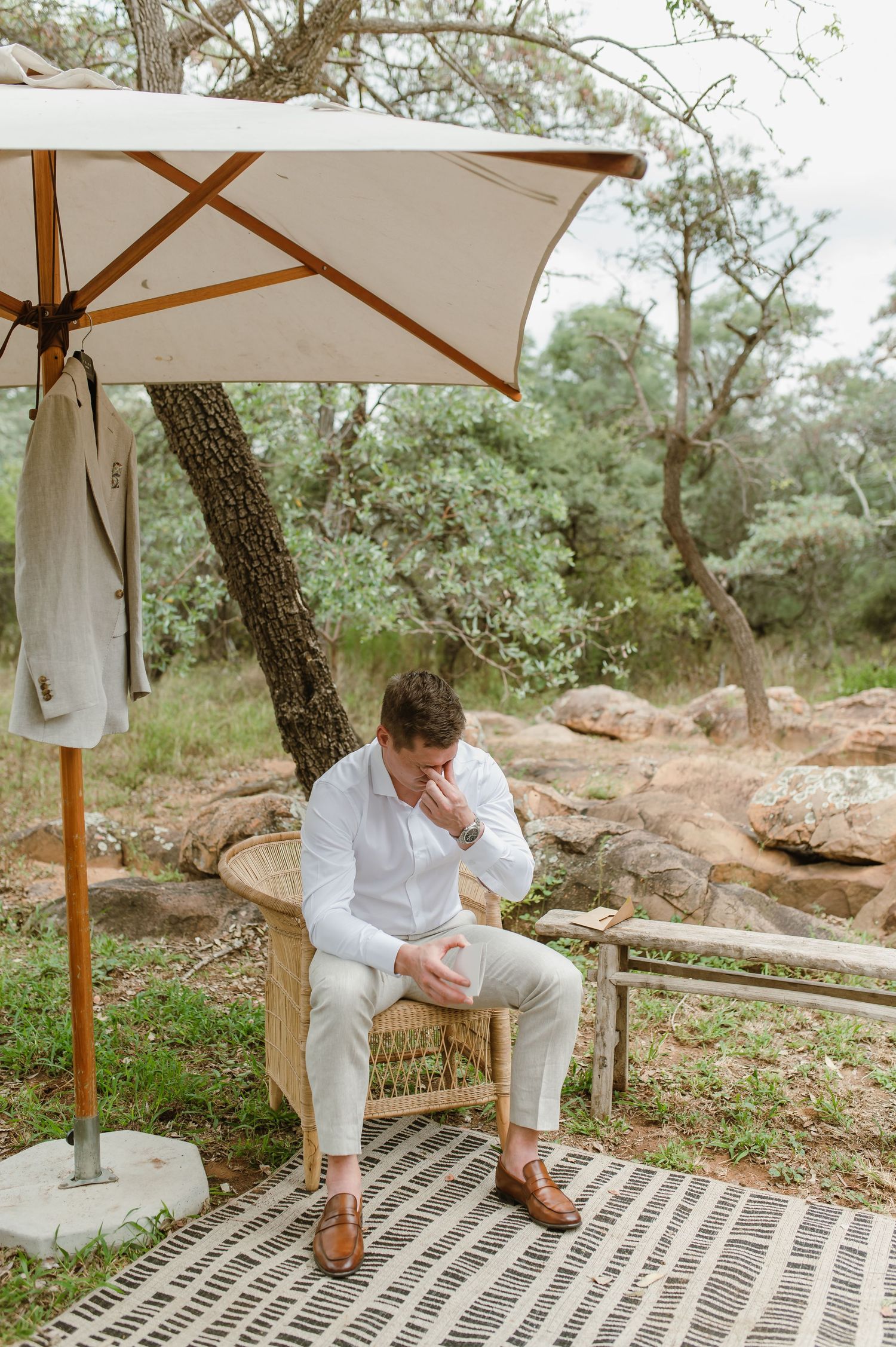 A serene outdoor patio setup with a white market umbrella and wicker chair against a natural rocky landscape.