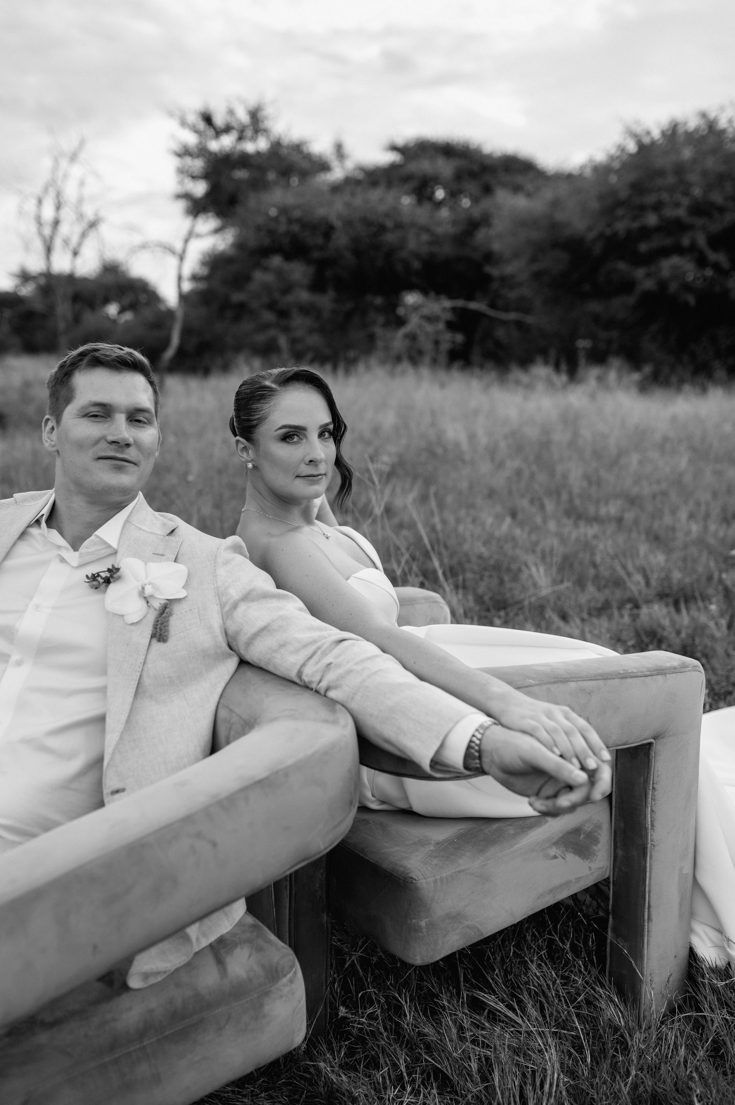 A black and white wedding photo of a couple sitting on an outdoor bench in a field.