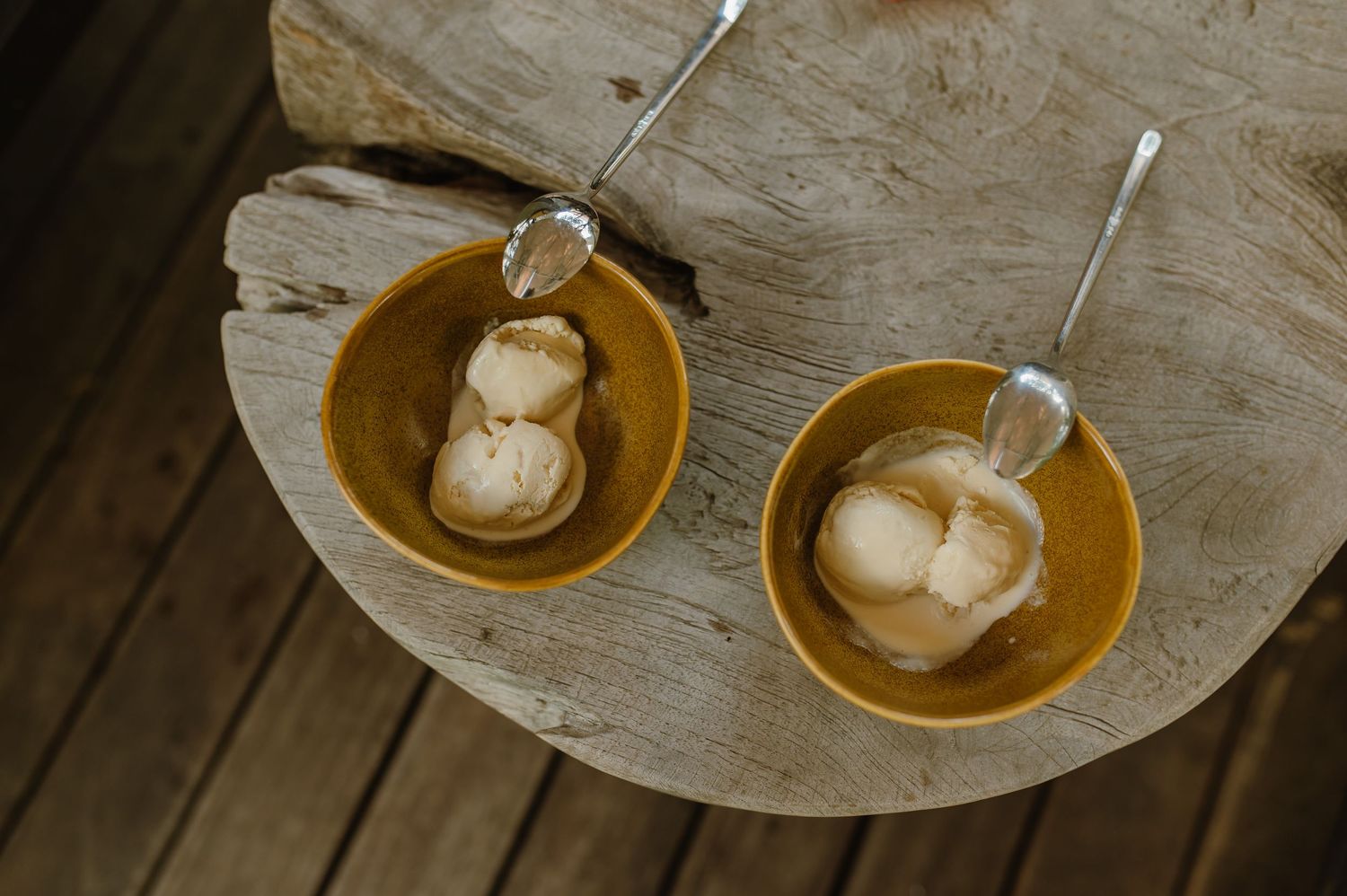 Two yellow bowls of vanilla ice cream with spoons on a rustic wooden surface.