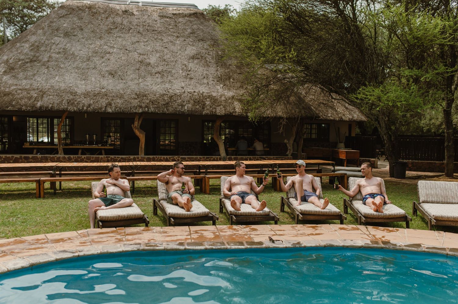 A row of outdoor swimming pools with thatched roof buildings and lounge chairs surrounded by lush greenery.