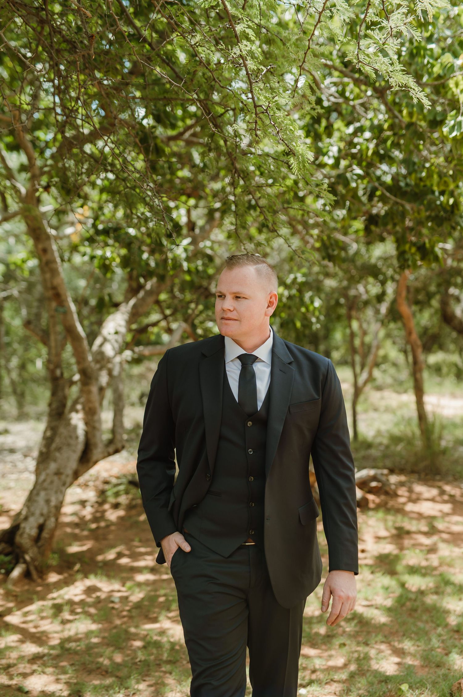 Wedding party members walking through a sunlit orchard in formal attire.