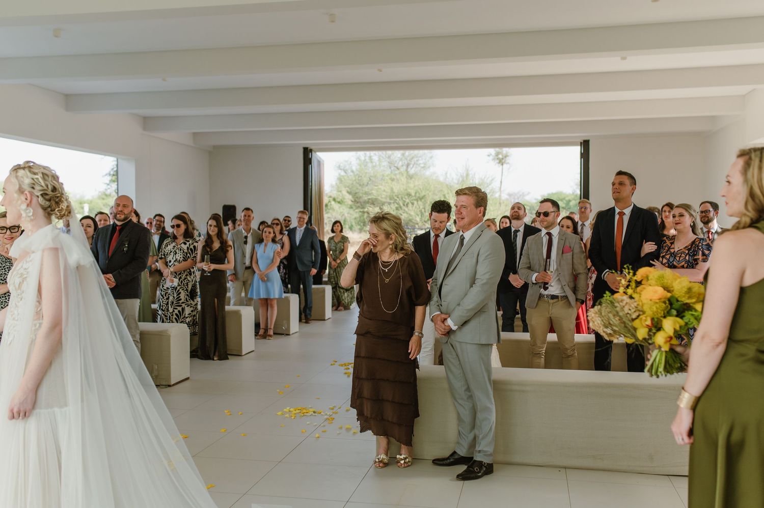 Wedding guests gather in a bright indoor venue with yellow floral arrangements.