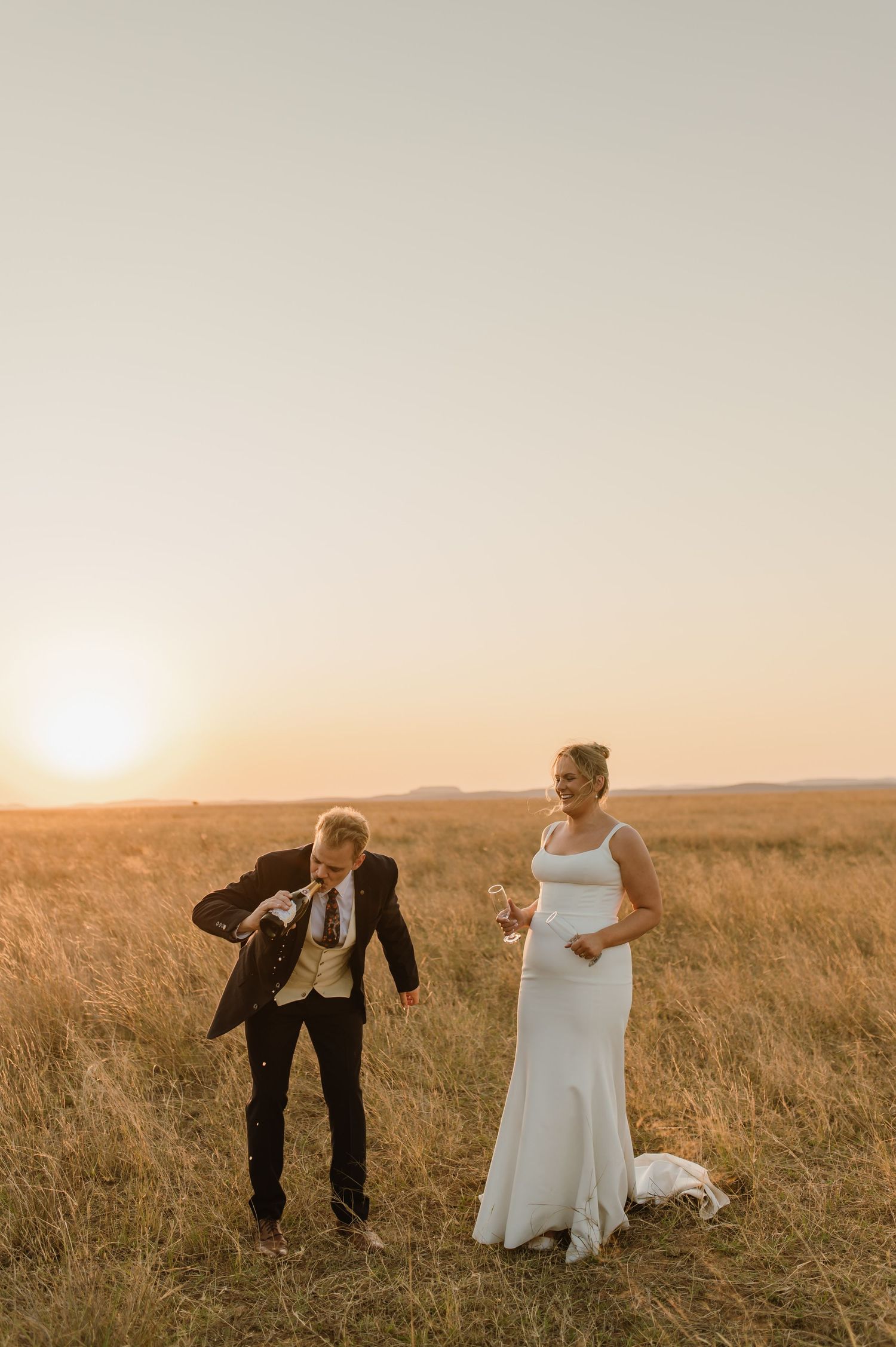Fun wedding poses captured in rustic field during golden hour.
