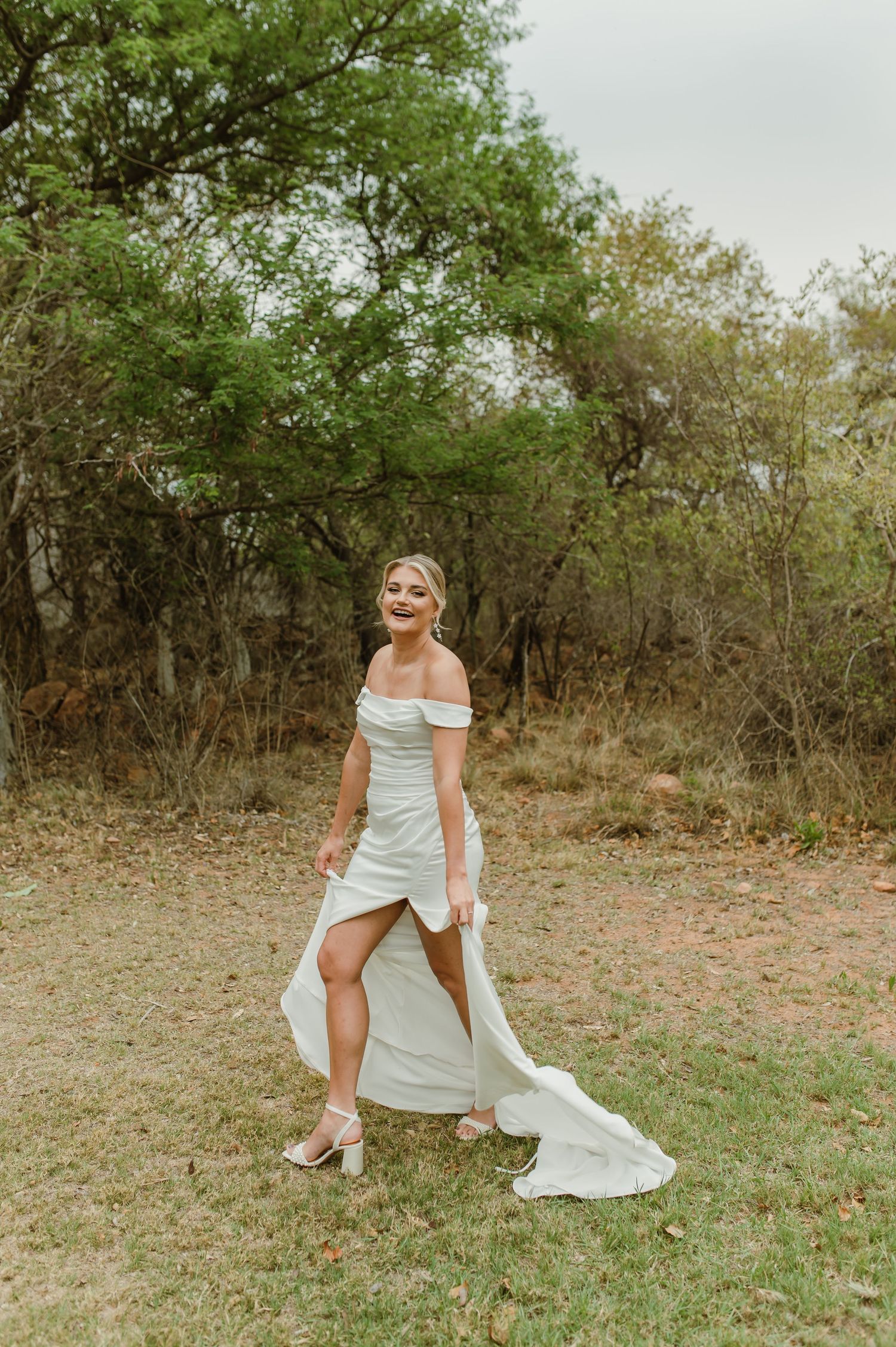 Elegant off-shoulder wedding dress with flowing train captured in natural outdoor setting.