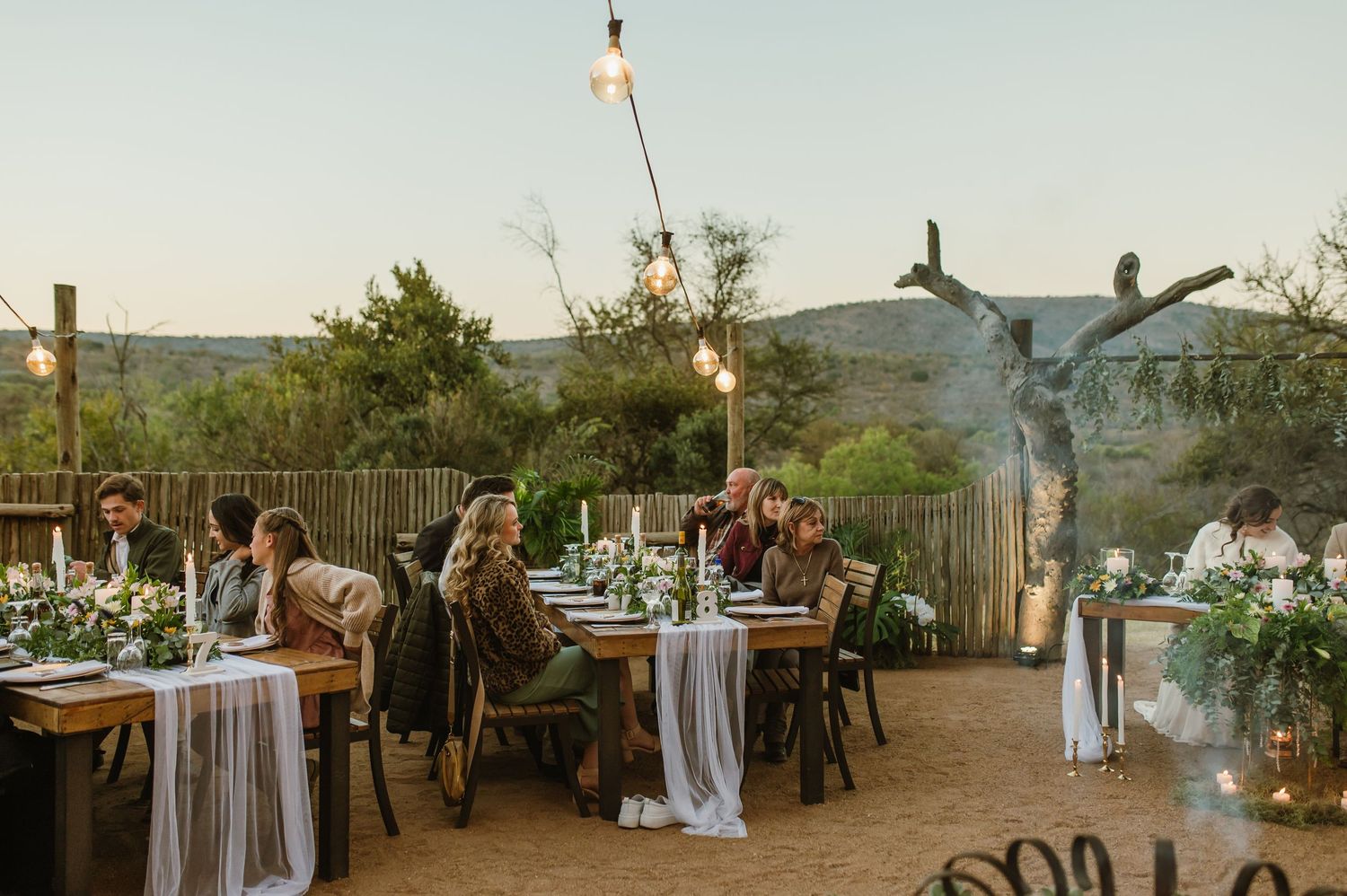 Wedding reception venue with rustic decor, string lights and white draped tables under open sky.