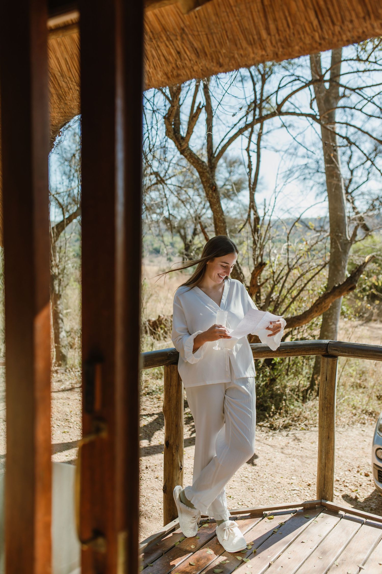 Figure in white dress walking along wooden deck surrounded by desert landscape and trees.