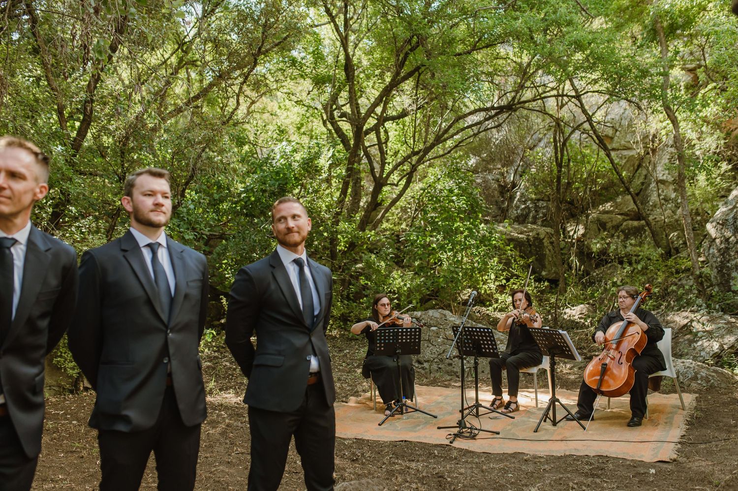 Wedding party members stand in formation during an outdoor forest ceremony.