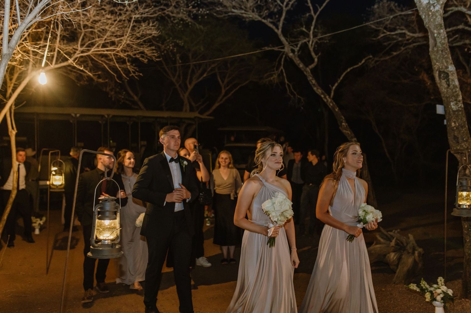 Nighttime outdoor event with guests gathered under trees and ambient lighting.