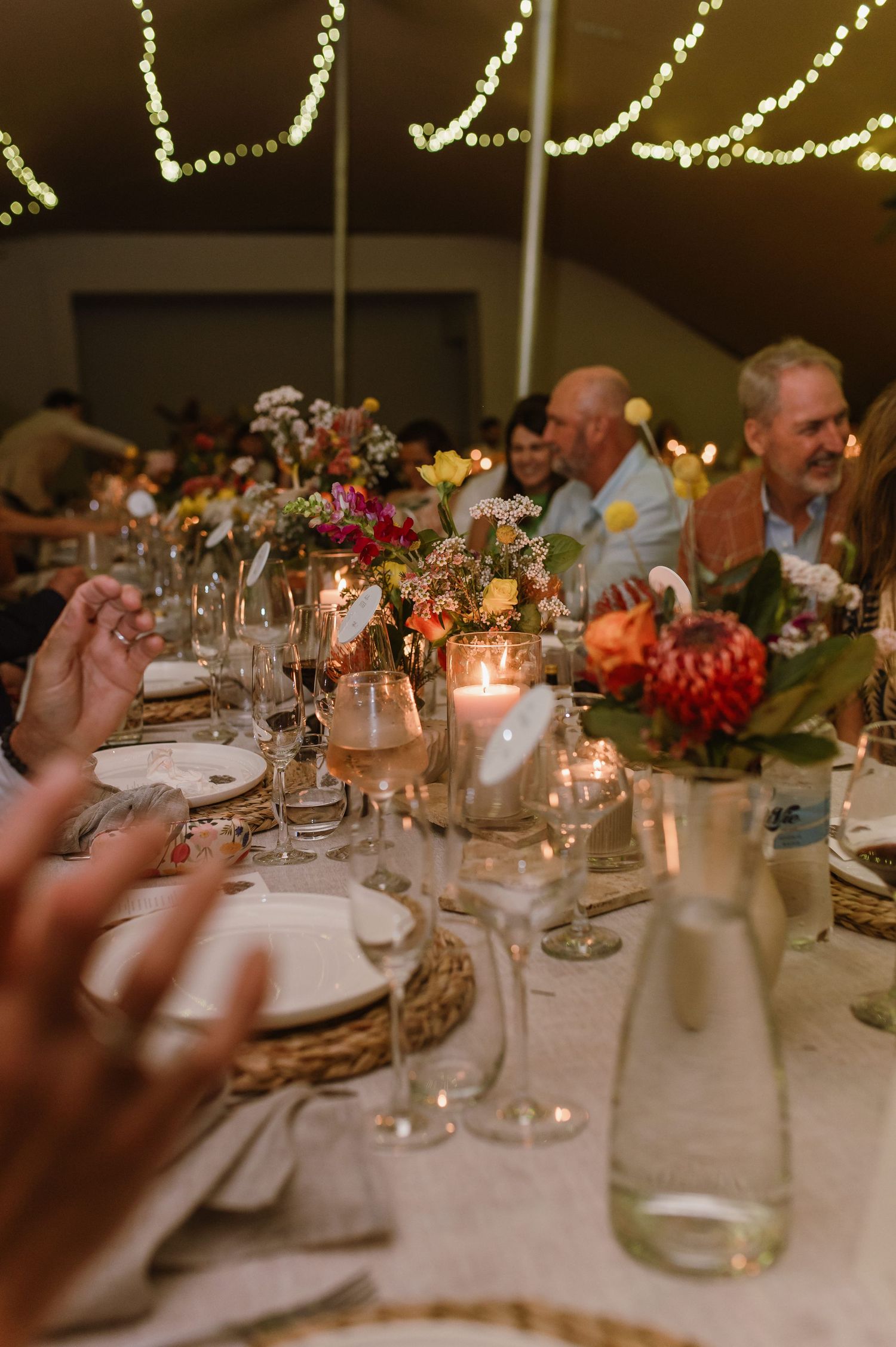 Elegant table settings with floral centerpieces and candles under string lights at a wedding reception.