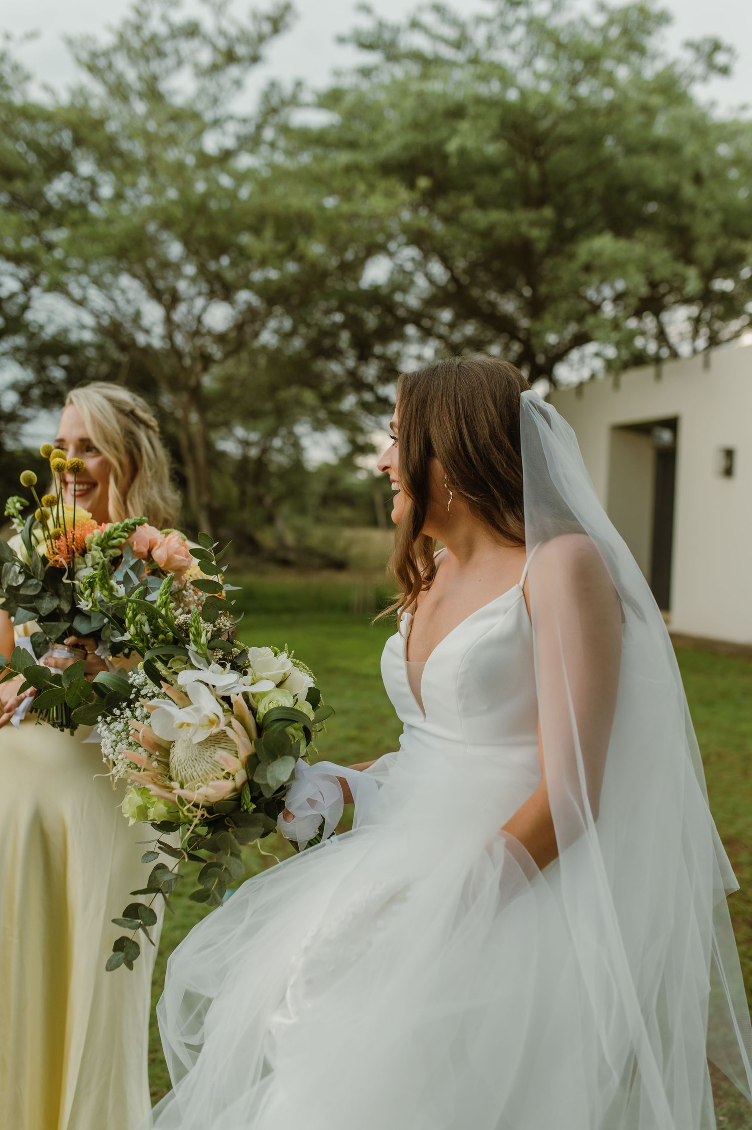 Elegant bridal portrait showcasing flowing white gown and vibrant bouquet against natural outdoor setting.