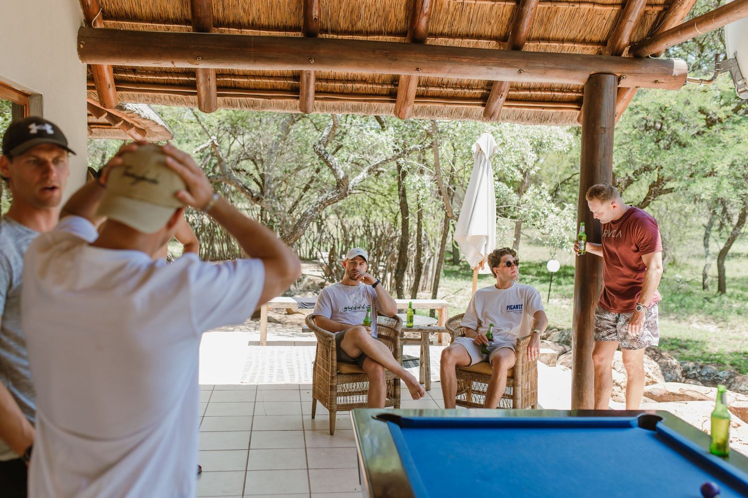 People socializing and playing billiards in a tropical outdoor setting.