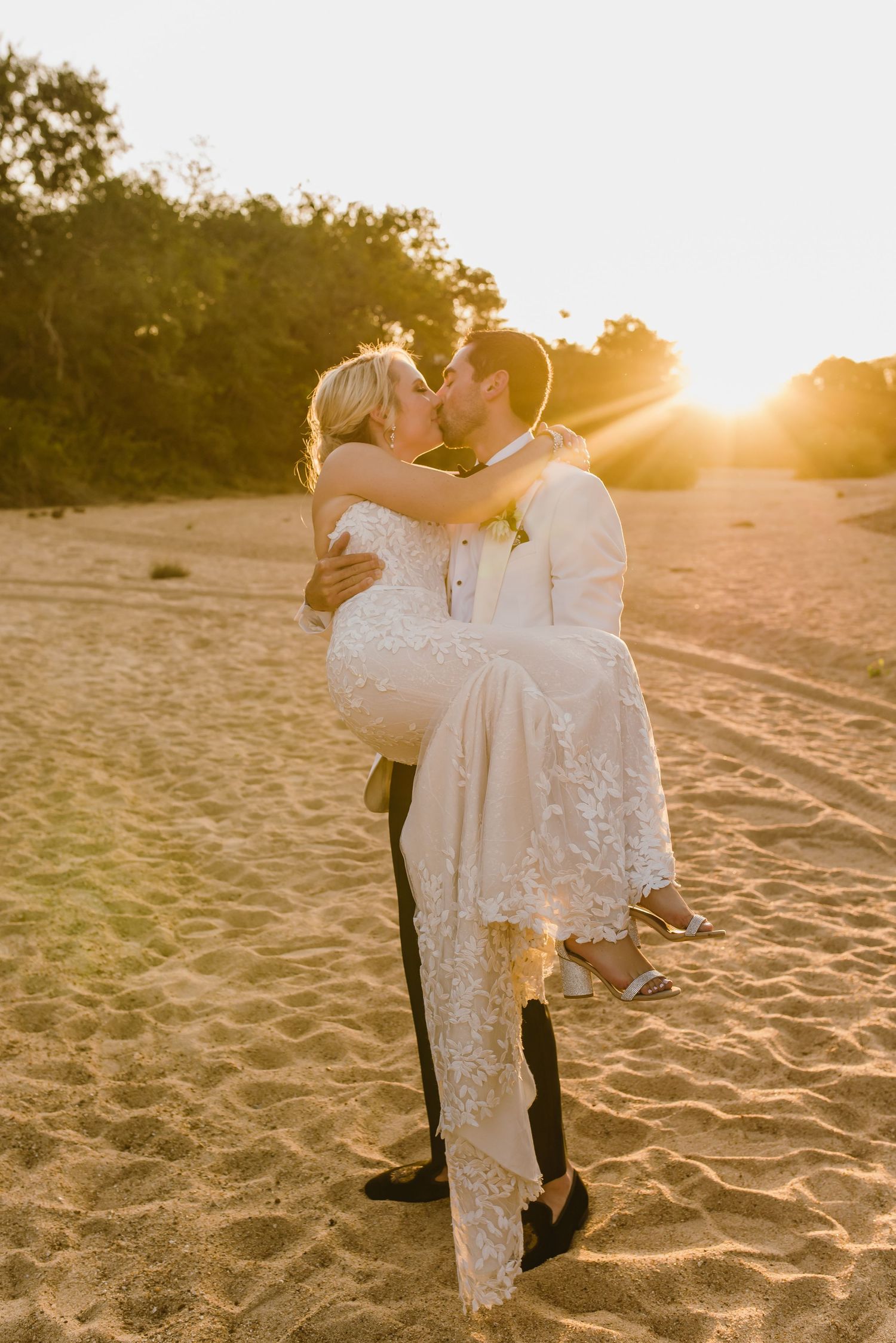 Intimate wedding moment captured on sandy beach during sunset.