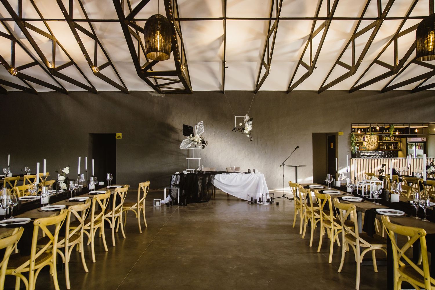 Panoramic view of a spacious reception hall with yellow chairs and rustic wooden beams.