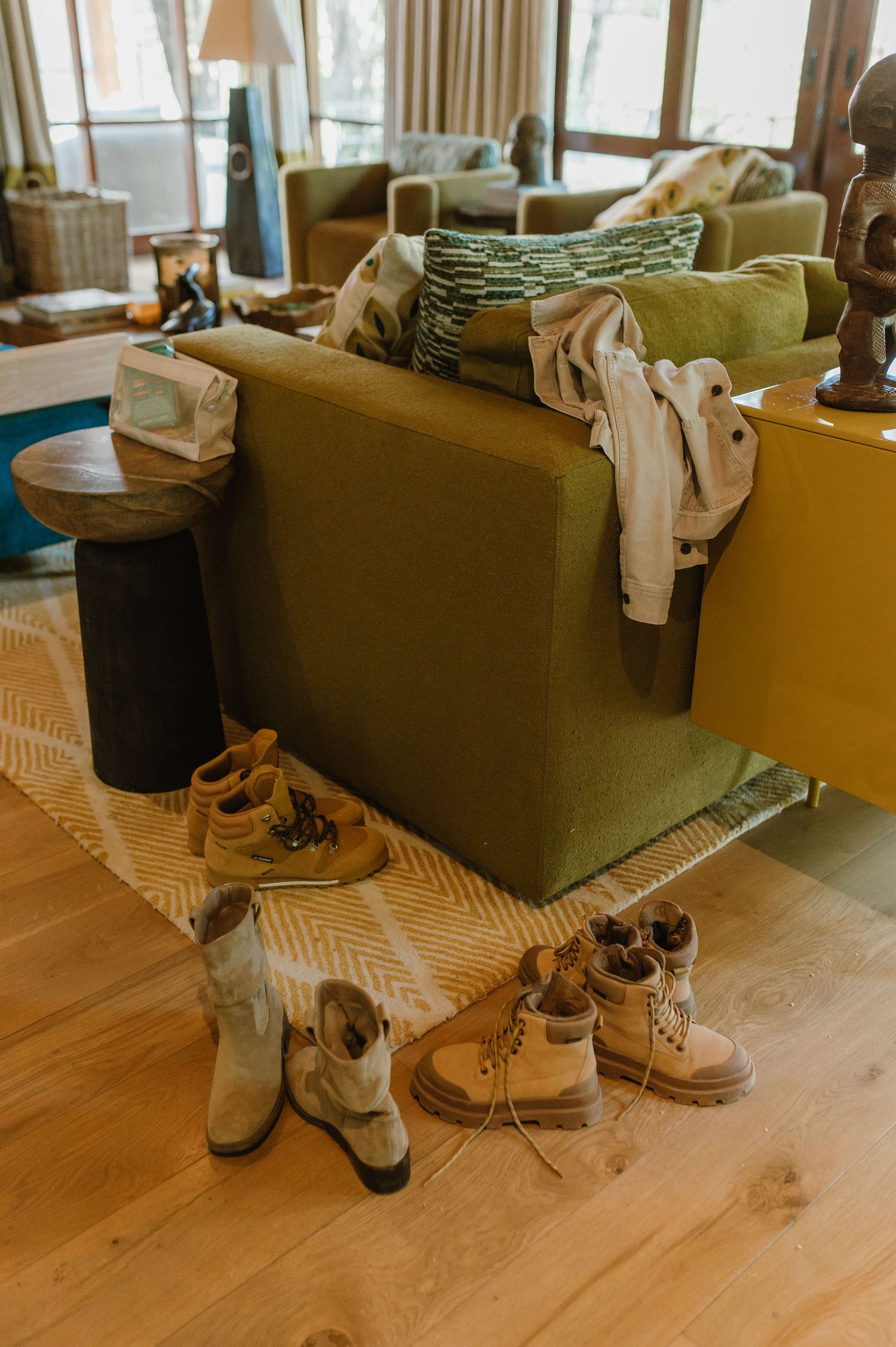 Hiking boots and shoes arranged on a rug beside a green sofa in a safari lodge living room.