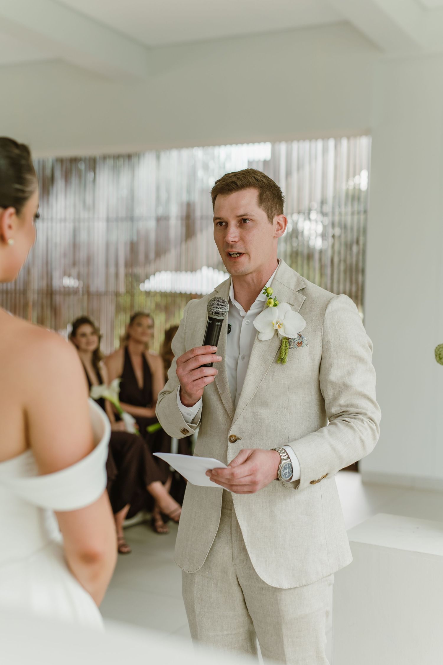 A couple exchanging wedding vows in a bright indoor ceremony space with guests watching in the background.