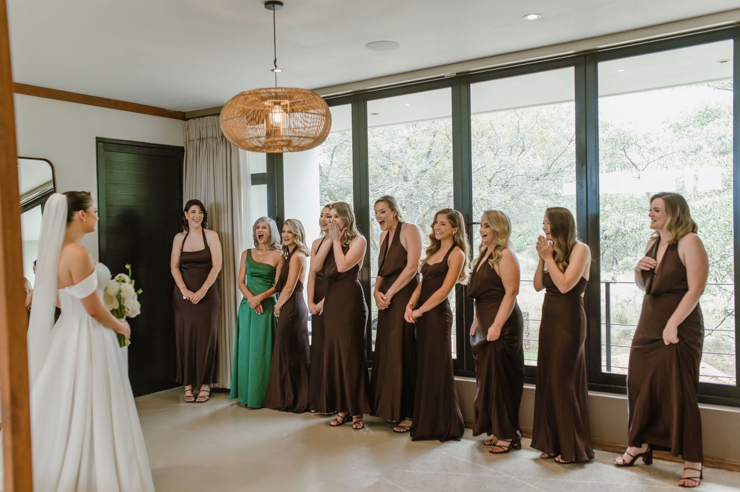 Wedding party in brown dresses watching bride in white gown in modern interior space.