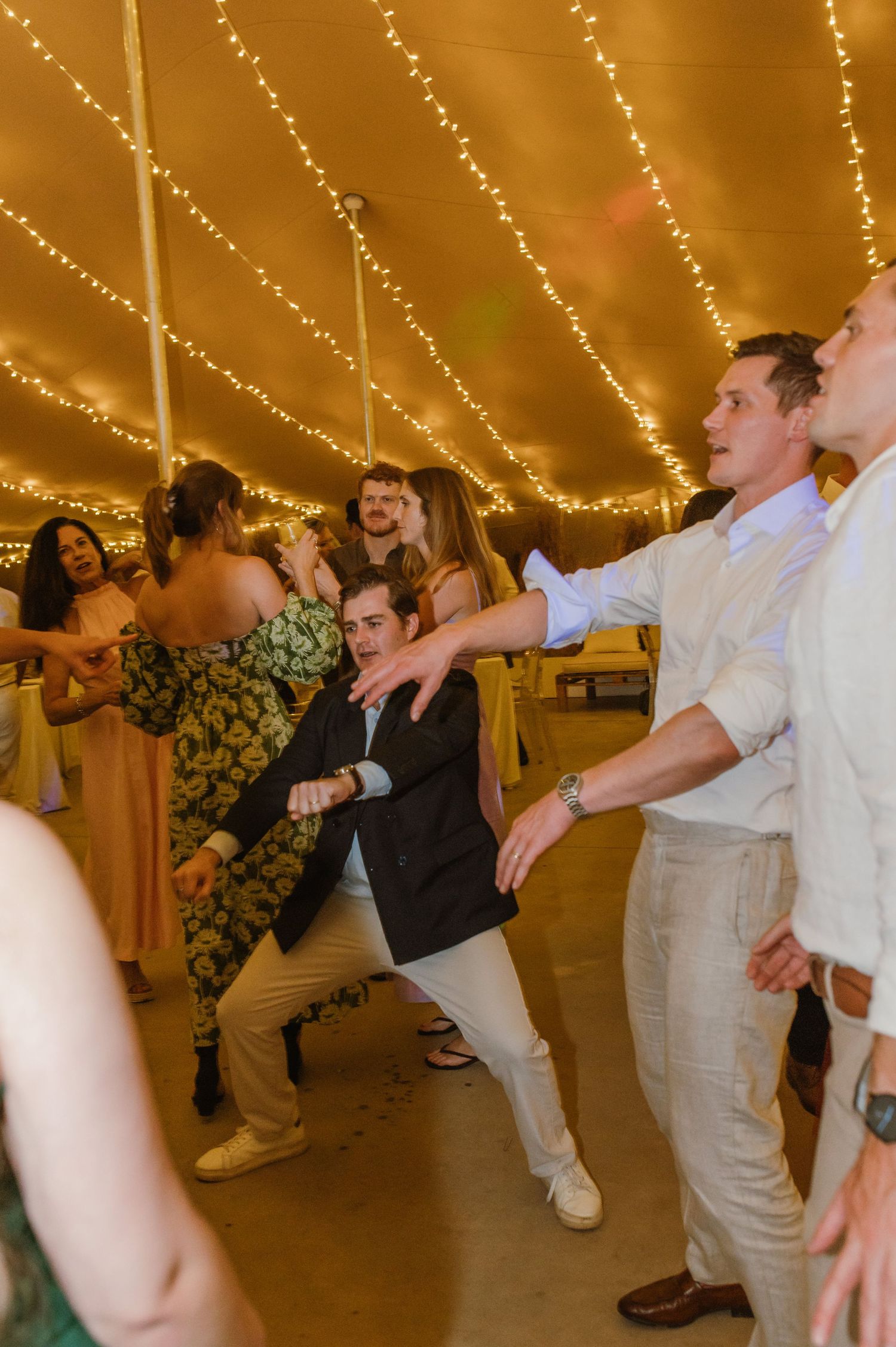 Wedding guests dancing and celebrating under string light canopy at reception.