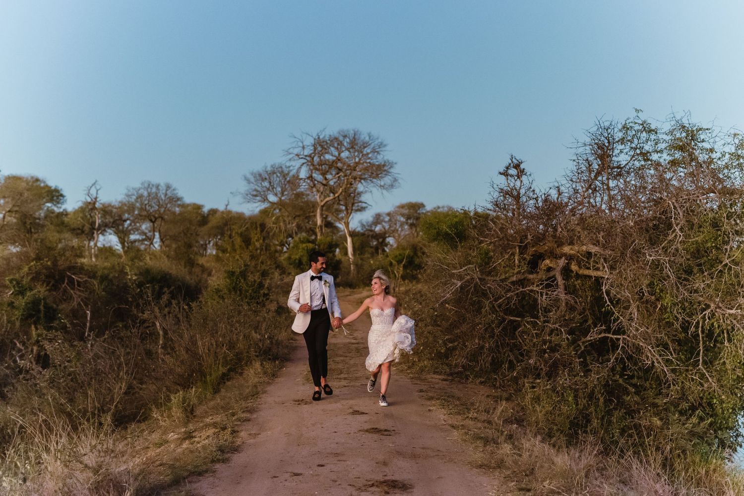 Couple walking down a scenic nature path near water at sunset.