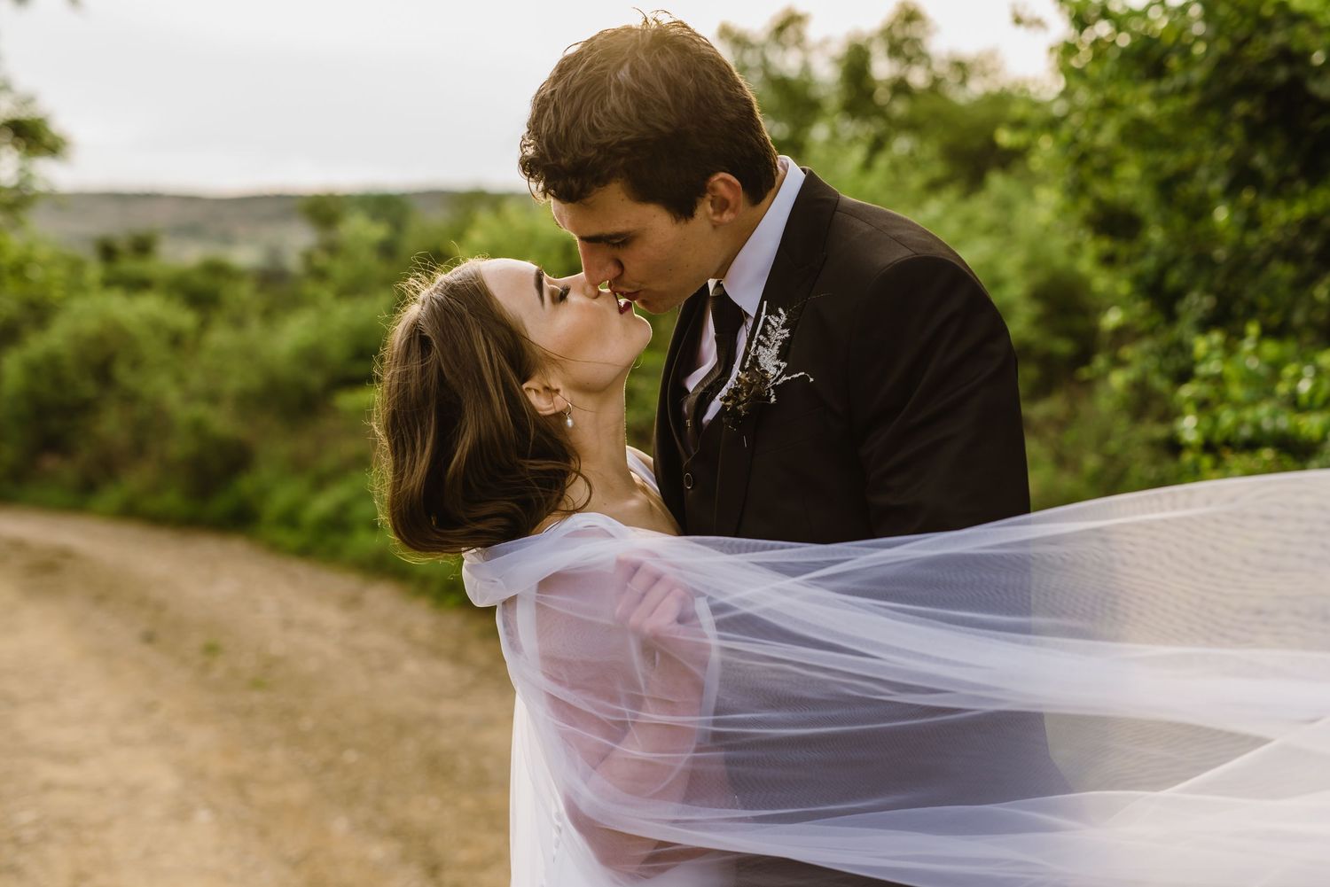 Wedding couple sharing intimate moment with flowing veil in garden setting.