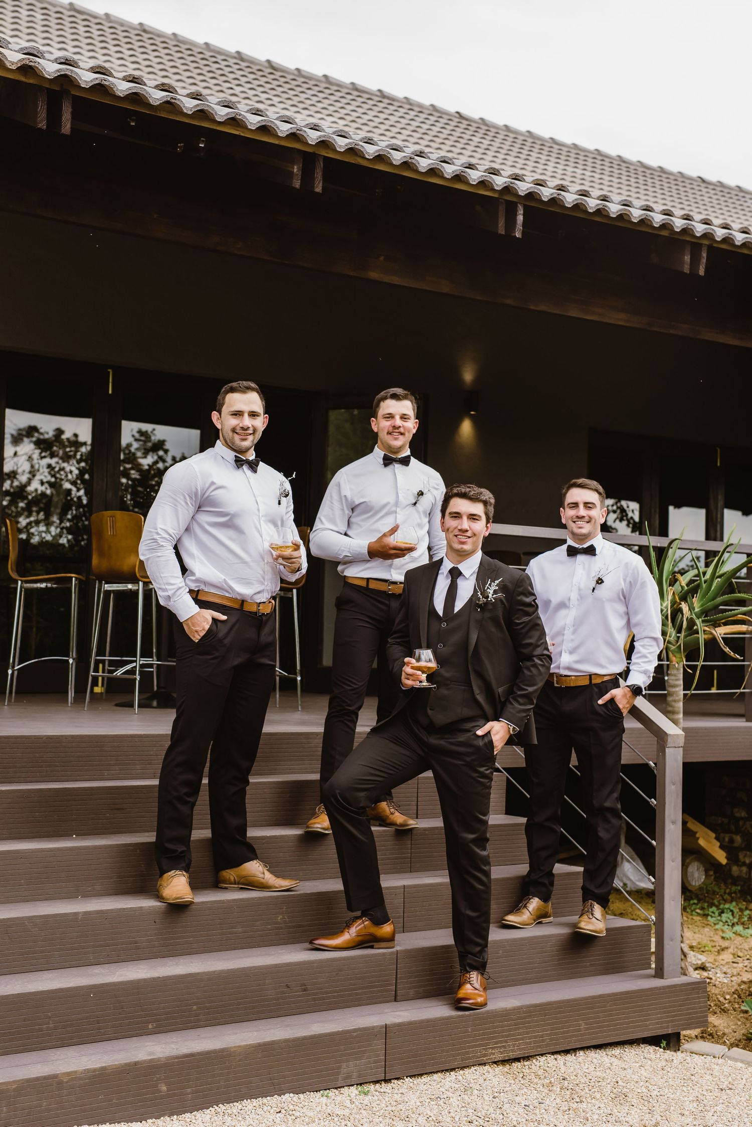 Wedding party members seated casually on outdoor wooden steps.