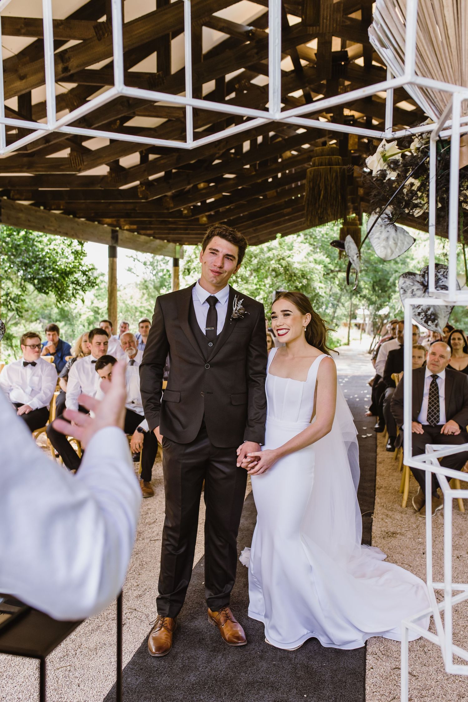 Wedding couple sharing joyful moments under a covered pavilion with white architectural details.