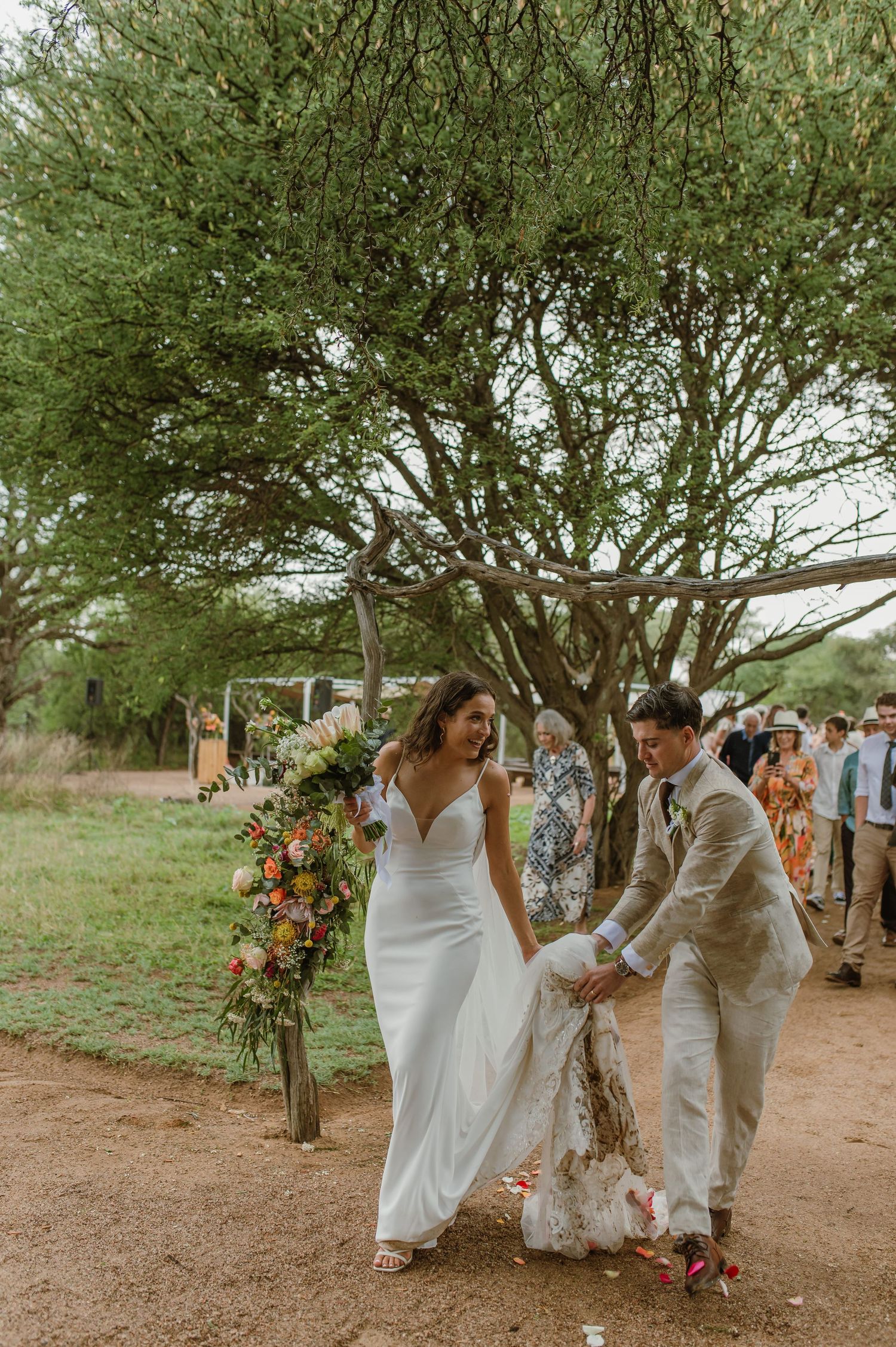 Wedding party walking along tree-lined path decorated with floral arrangements.