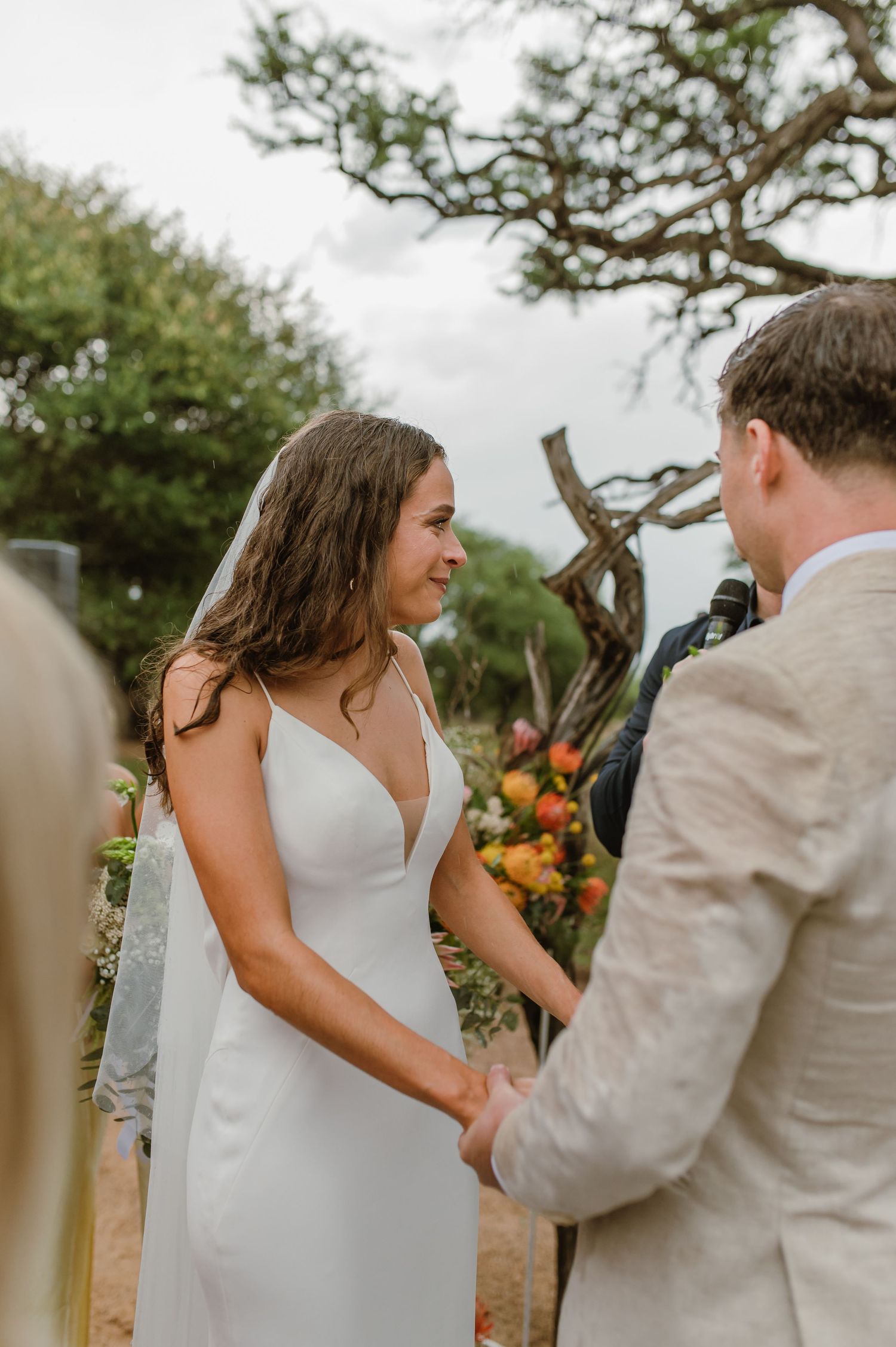 A couple shares an intimate moment during their outdoor wedding ceremony under a gnarled tree.