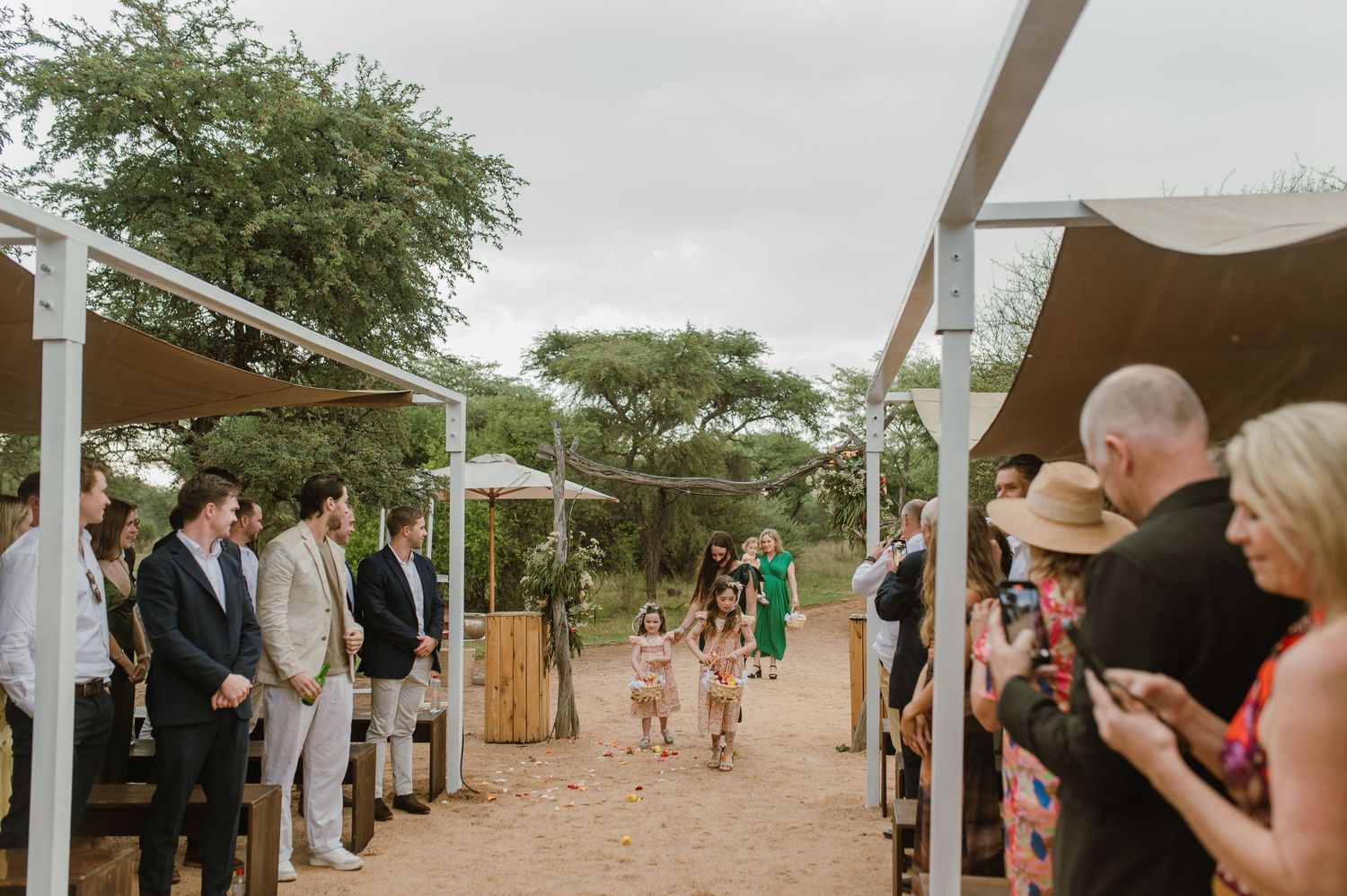 Guests observe a wedding ceremony under white canopy structures in an outdoor desert setting.