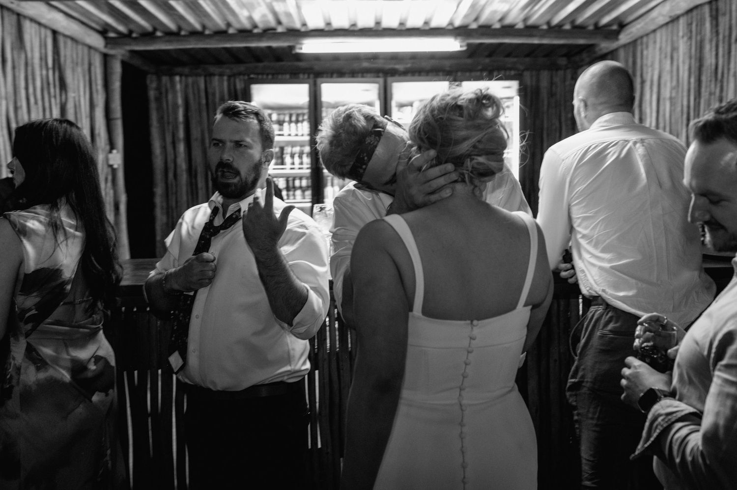 Black and white photo of wedding guests mingling in a covered outdoor space.