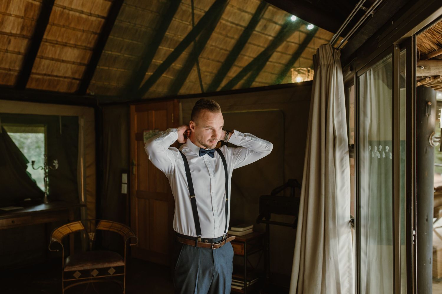 Person getting dressed in formal attire inside rustic room with natural lighting.