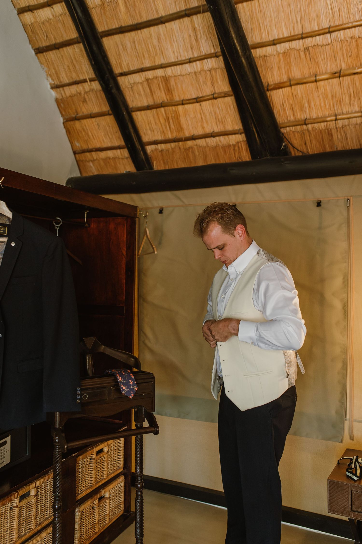 Someone getting dressed in a room with thatched roof and wardrobe storage.