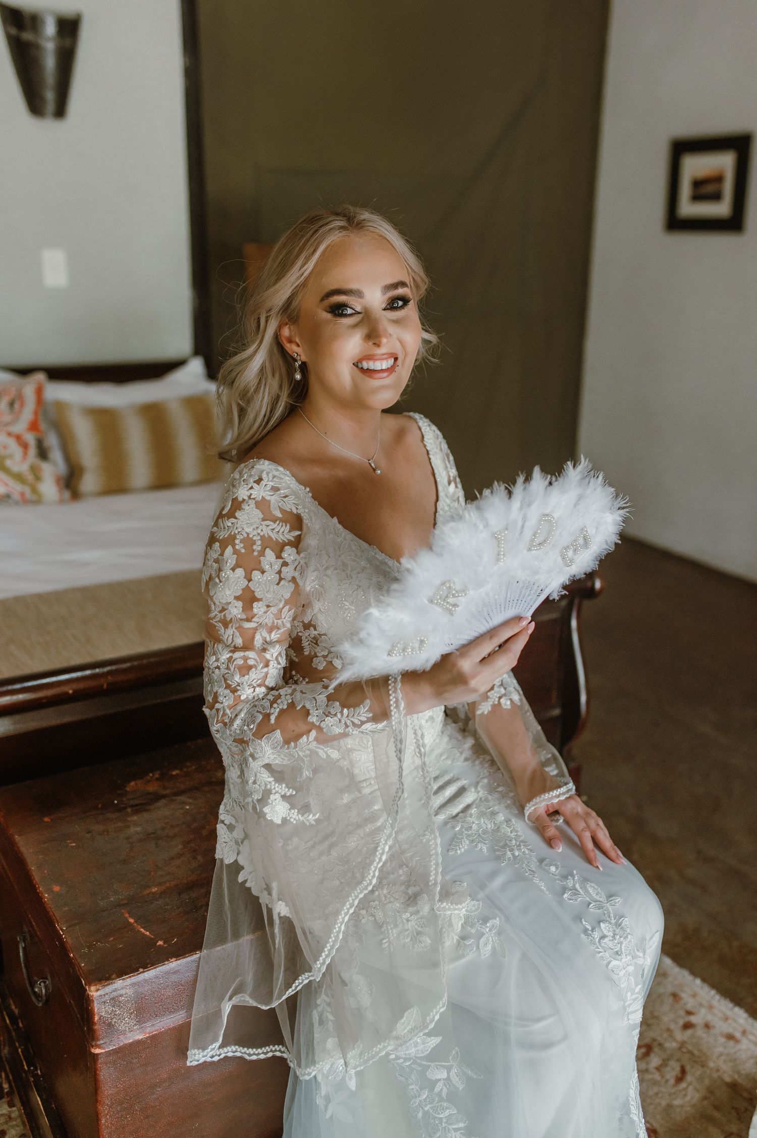 A wedding dress with delicate lace sleeves and a white feather fan accessory.