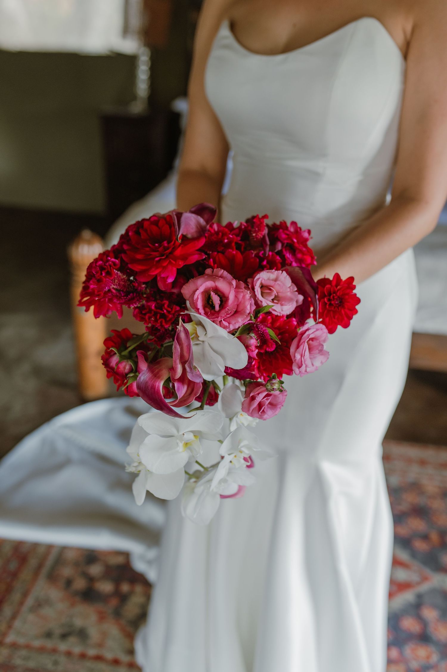 Close-up details of a stunning red and white bridal bouquet with orchids against a white wedding dress.