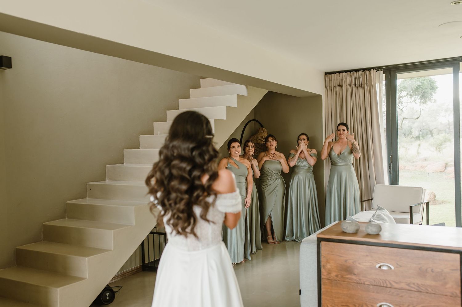 Bridesmaids in matching sage dresses share an emotional moment on modern white stairs.