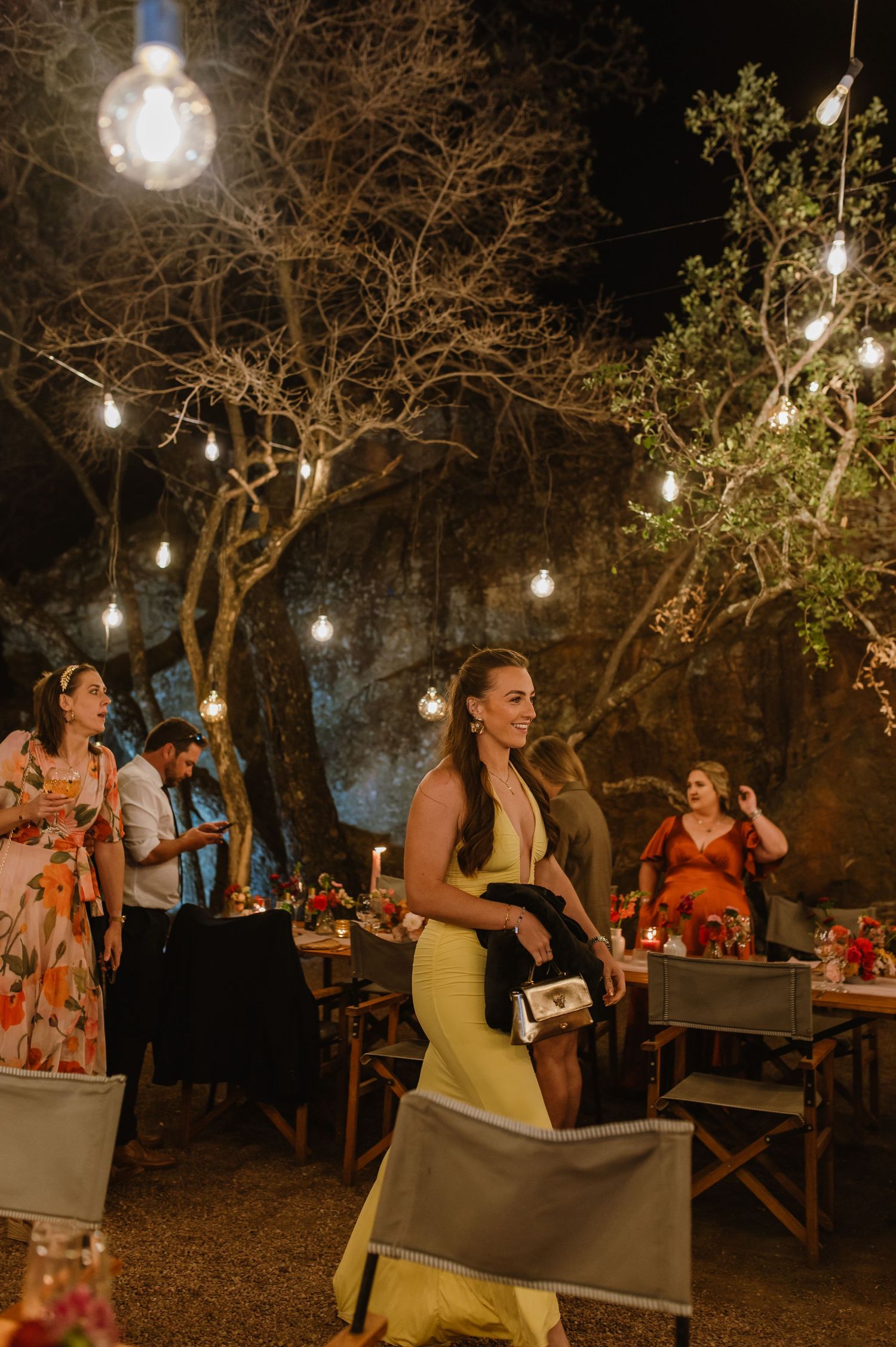 Outdoor wedding reception at night with string lights illuminating wooden tables and guests enjoying dinner.