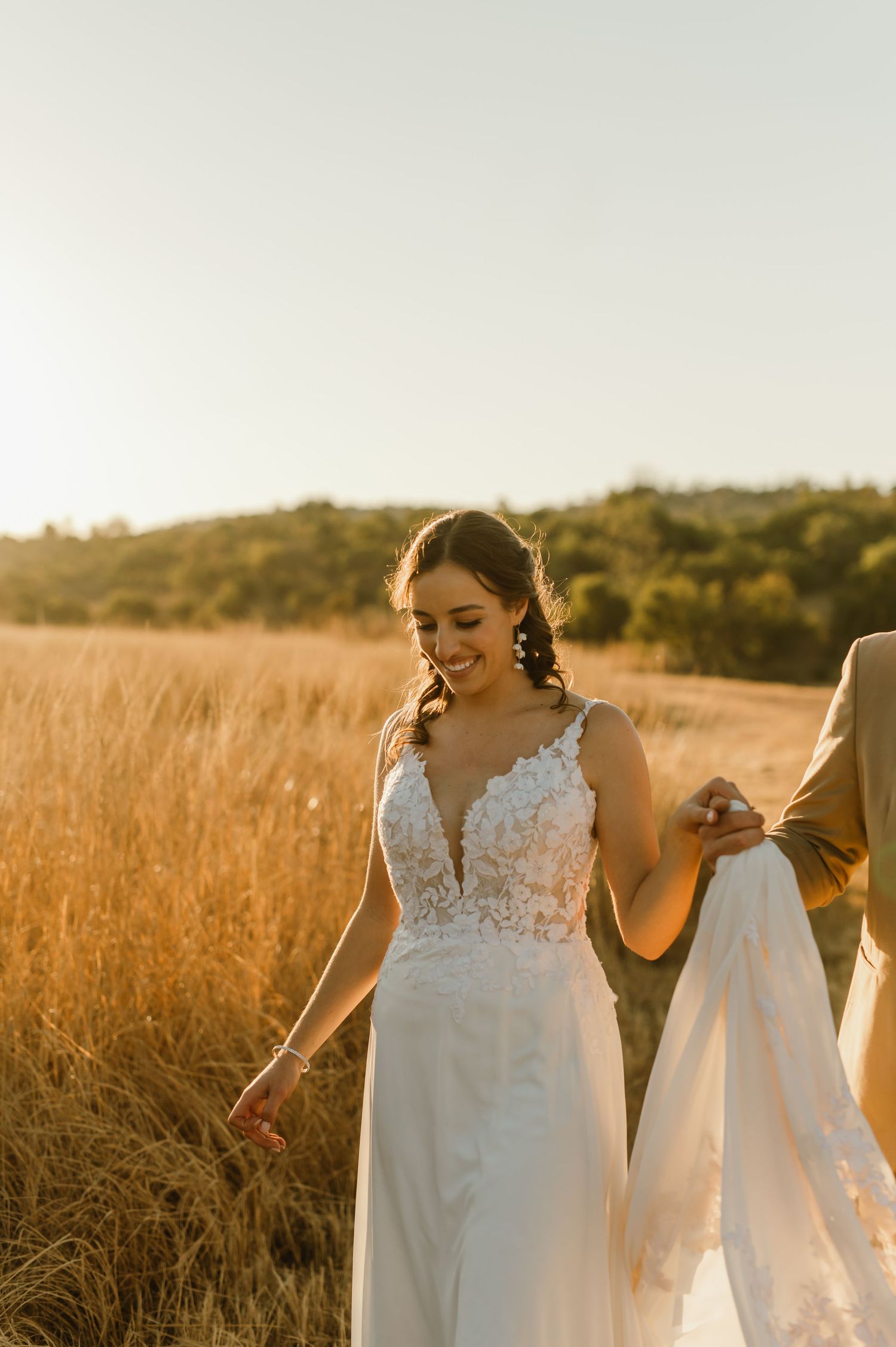 People in white dresses walk through golden grass during sunset.