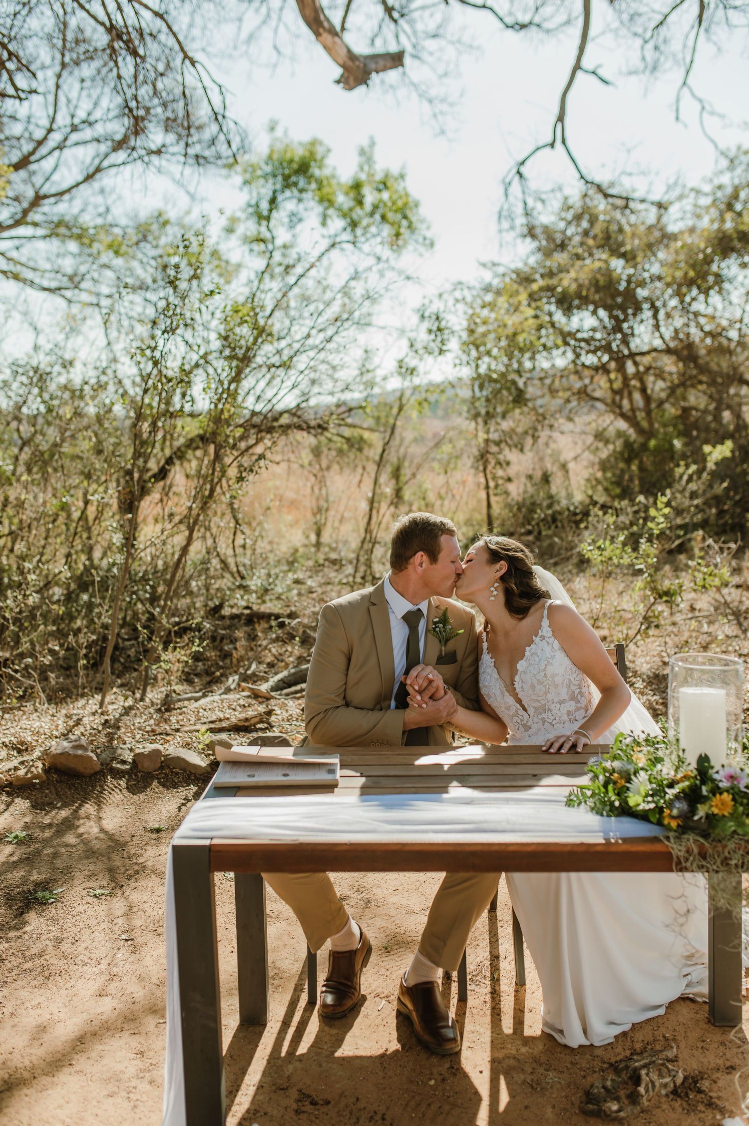 Couple shares intimate moment at rustic wooden table during desert wedding ceremony.