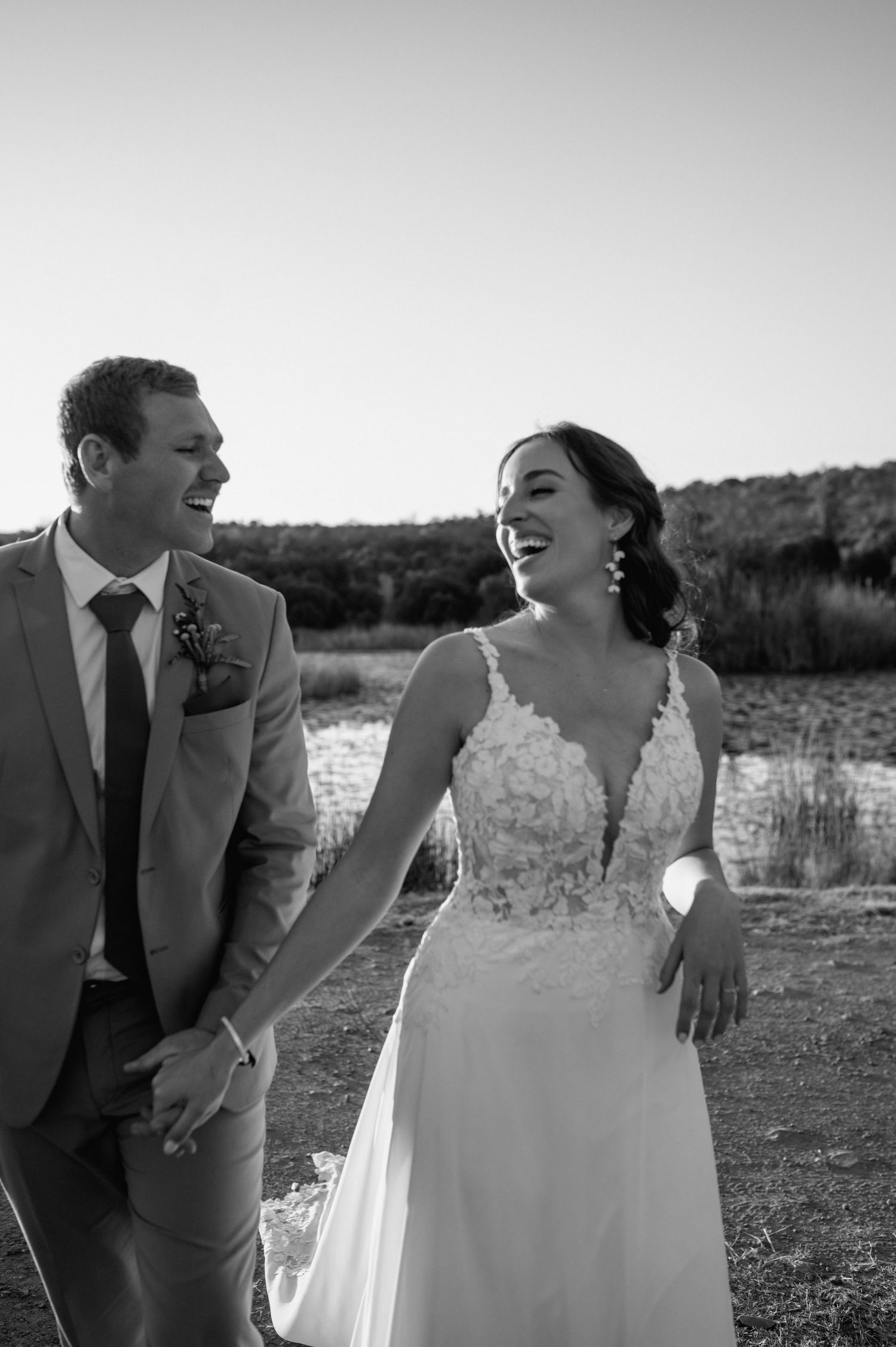 Black and white wedding portraits showing joyful candid moments by the lake.