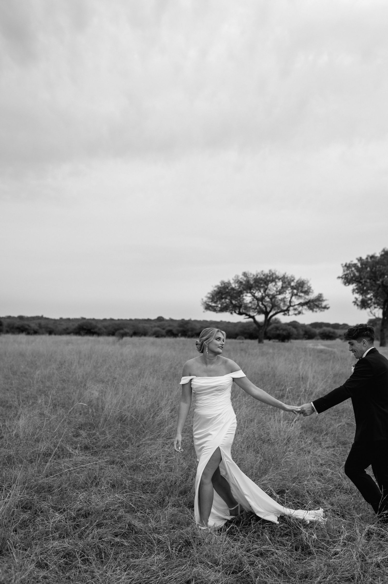 Black and white wedding photos of a couple dancing playfully in a rustic field setting.