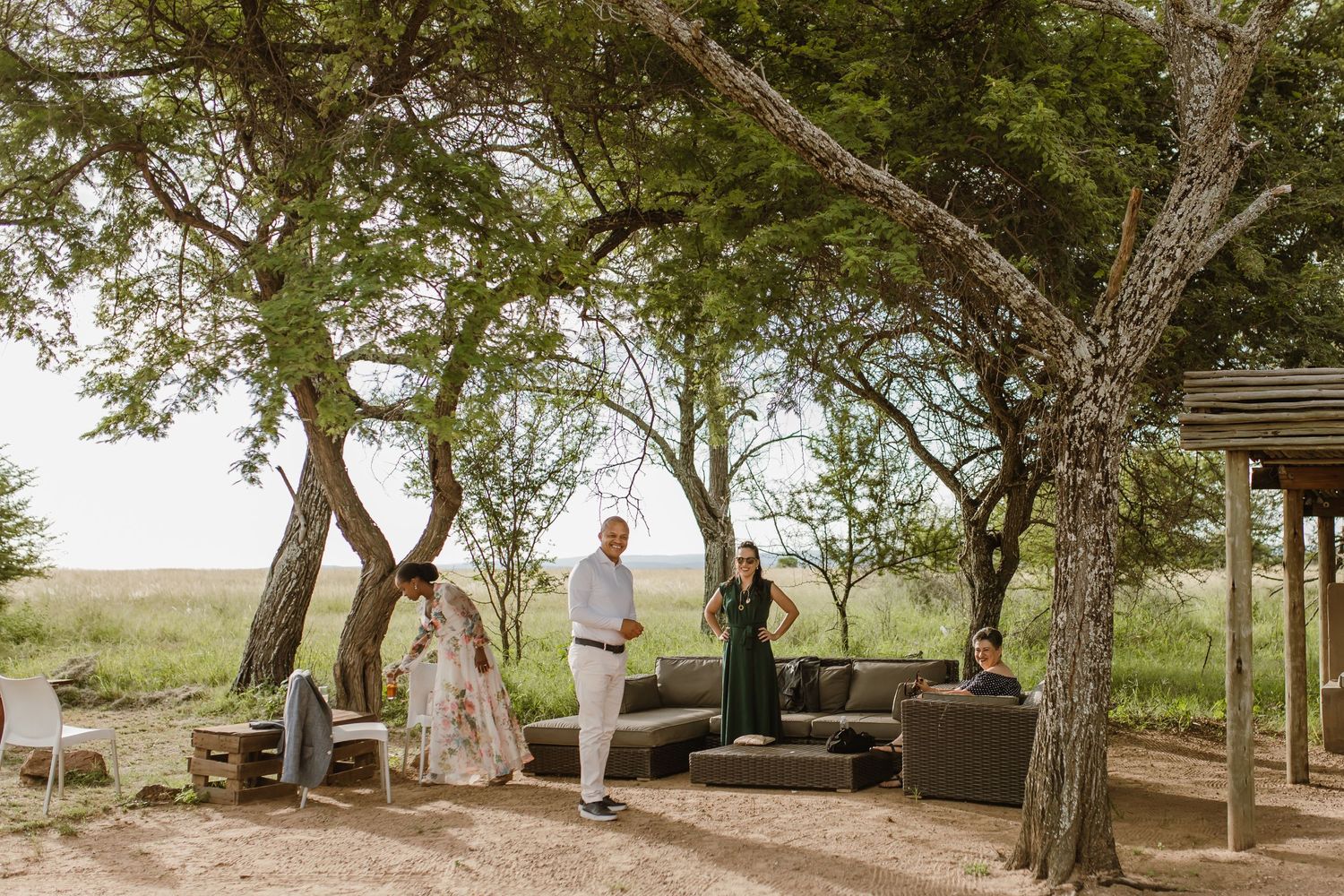 An intimate outdoor wedding ceremony takes place under shady trees on a sunny day.