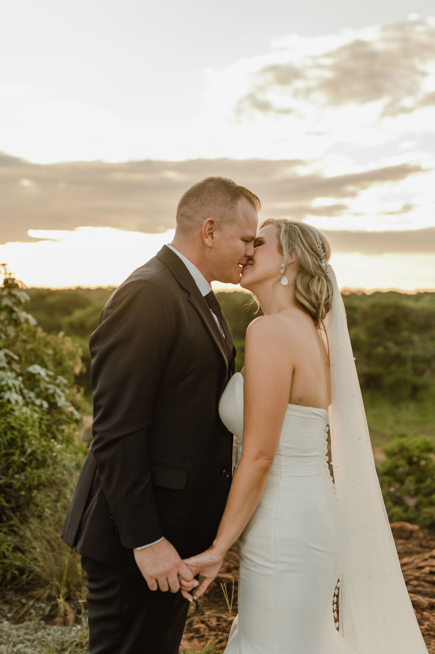 Newlyweds share an intimate kiss during golden hour in a natural outdoor setting.
