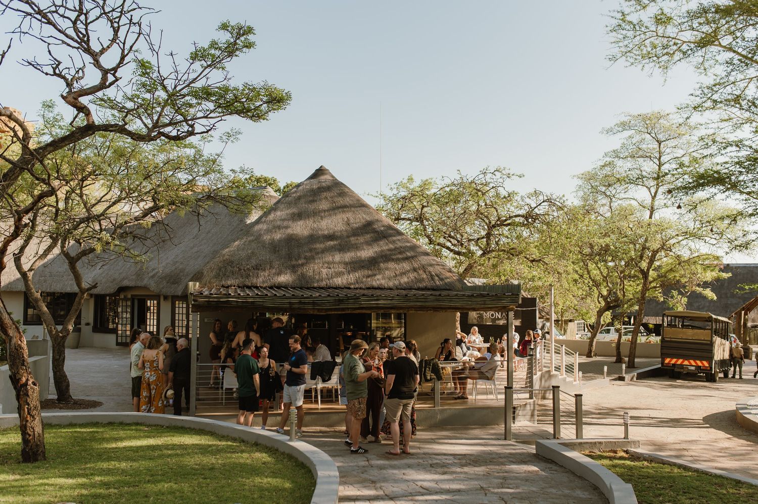 Panoramic view of a safari lodge with thatched roofs surrounded by acacia trees.
