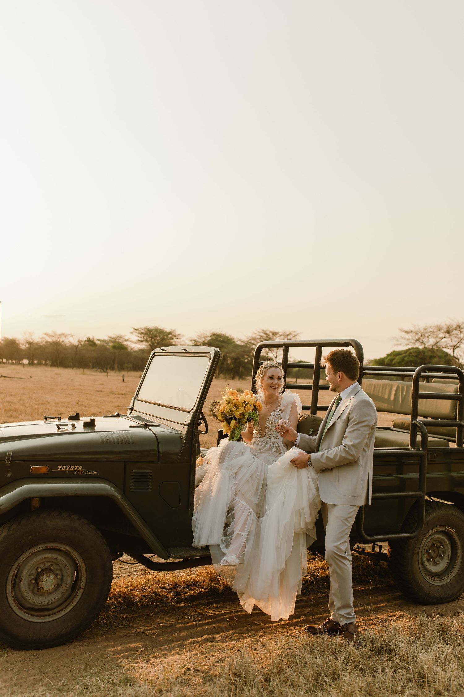 Wedding couple poses beside vintage Land Rover during golden hour photoshoot.