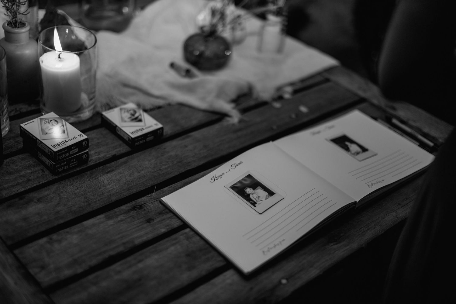 Candle illuminates guest book and wedding details on rustic wooden table.