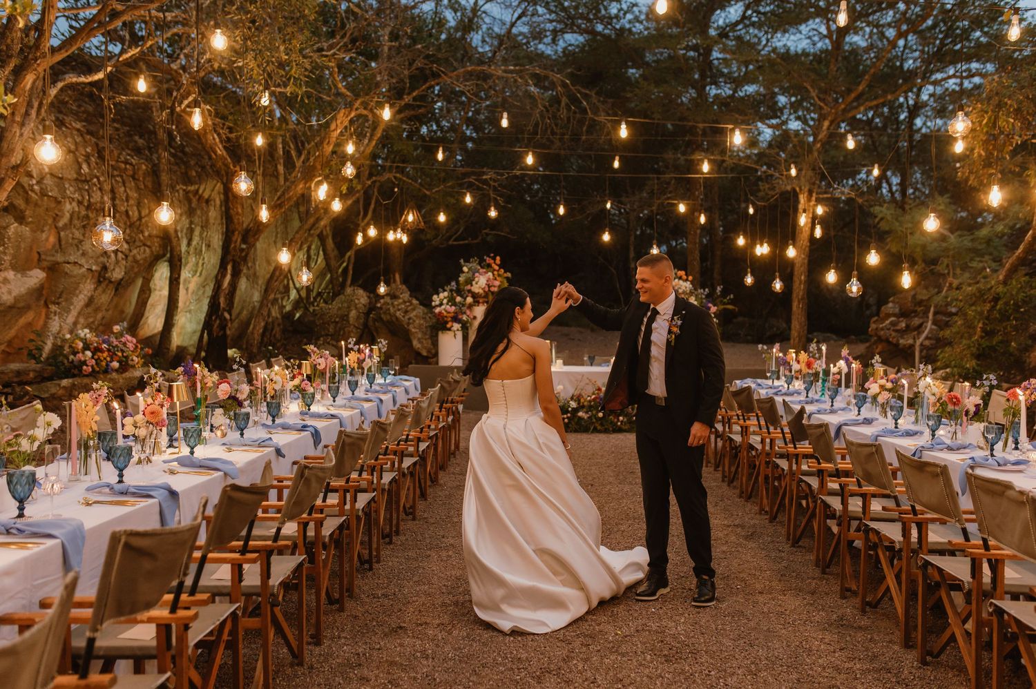 Bride and groom dancing between elegantly set reception tables under string lights.