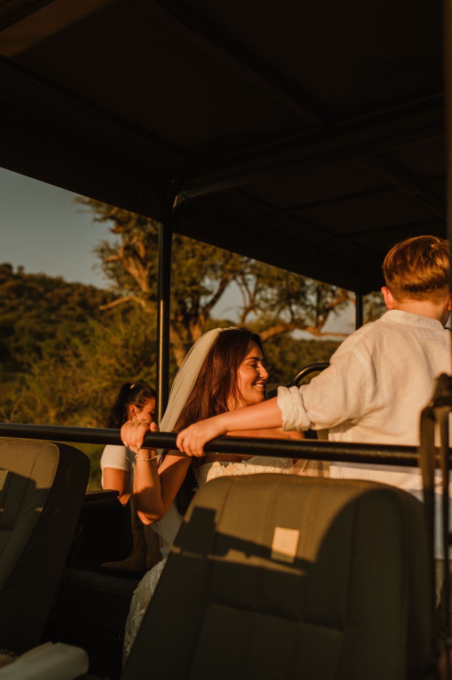 Bride in veil smiling aboard open safari vehicle at sunset during wedding day adventure.